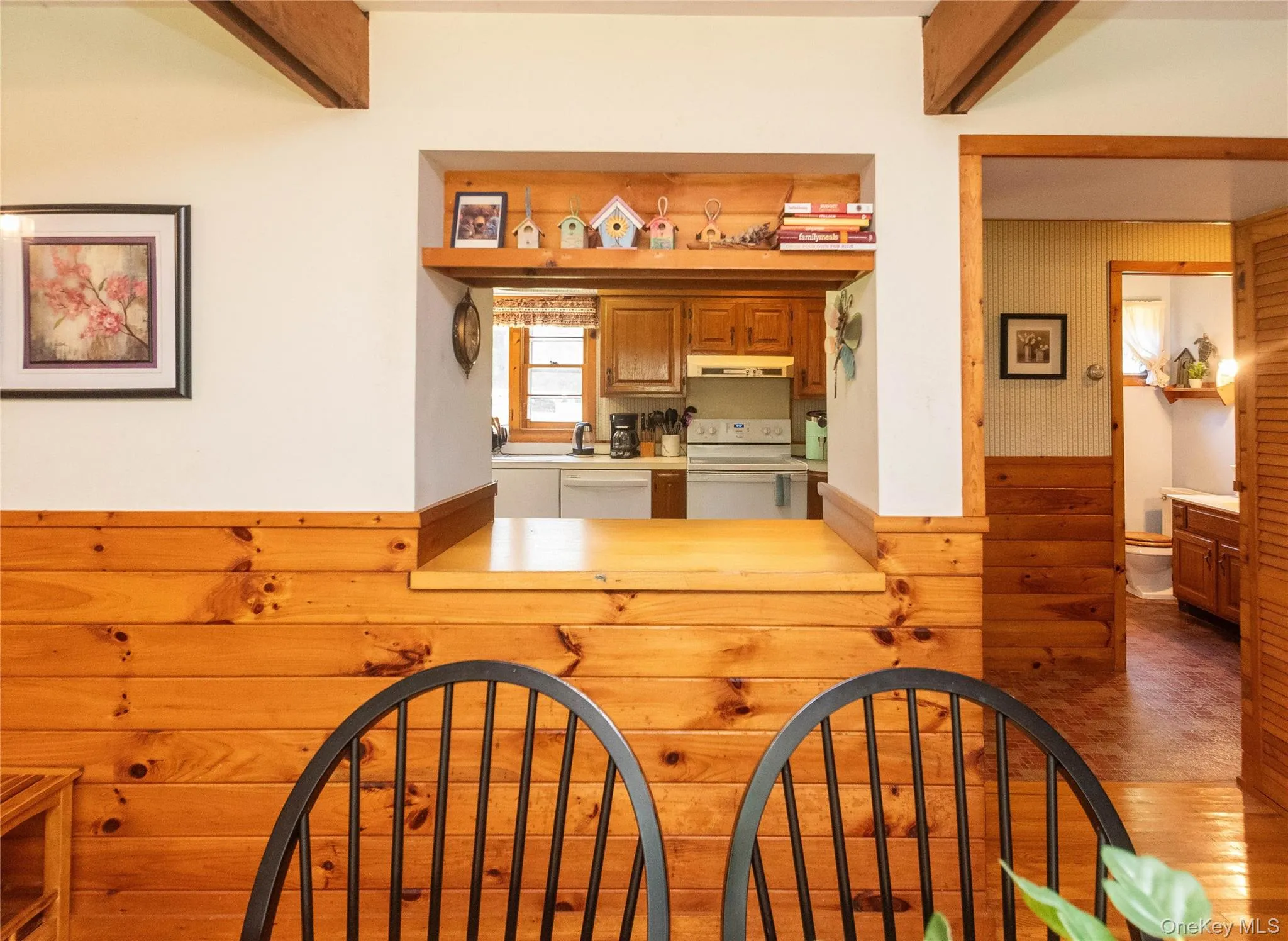 Kitchen featuring white appliances, beamed ceiling, light countertops, wood finished floors, and brown cabinets Kitchen featuring white appliances, beamed ceiling, light countertops, wood finished floors, and brown cabinets