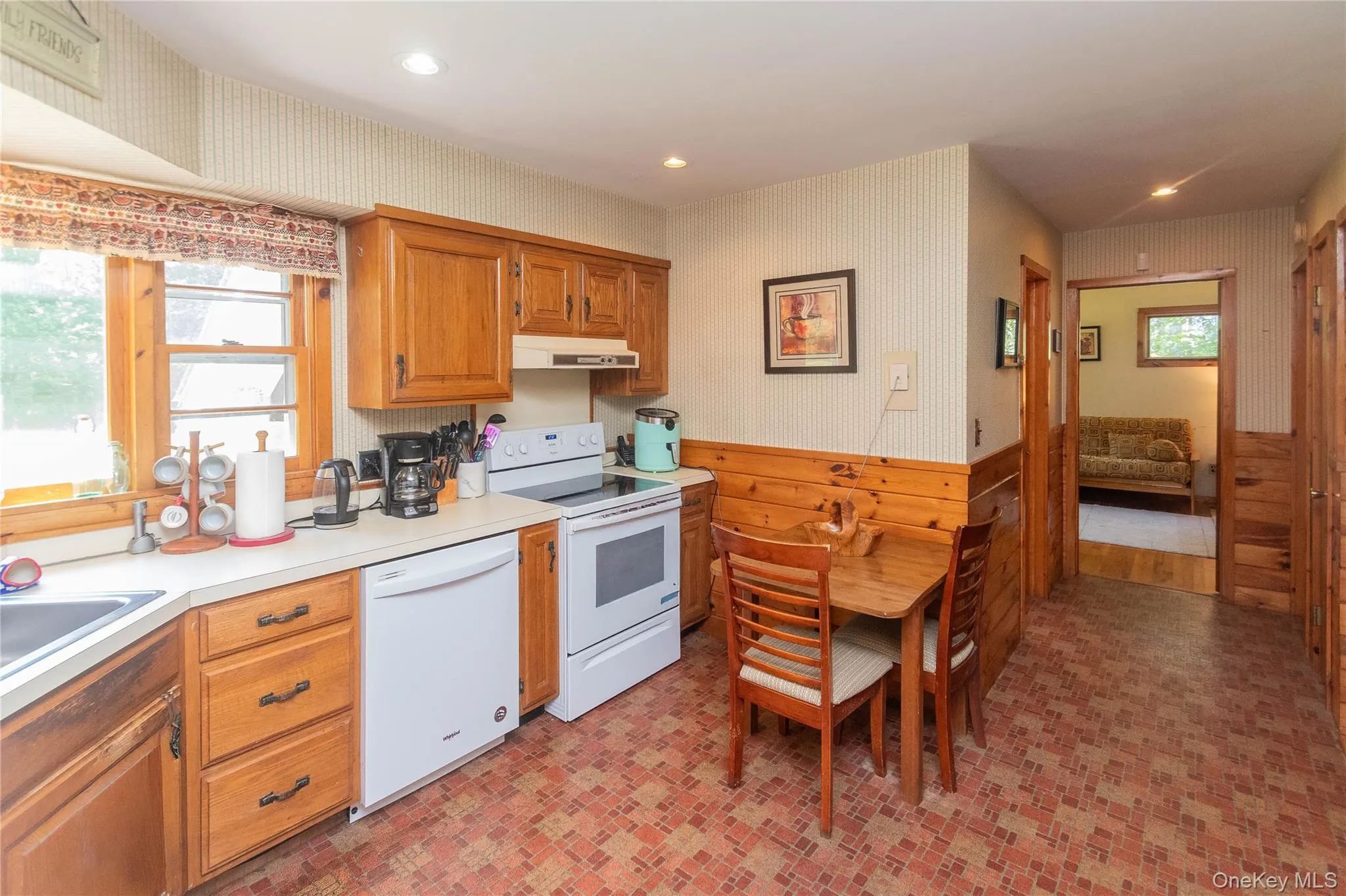 Kitchen featuring wallpapered walls, white appliances, a wainscoted wall, light countertops, and brown cabinets Kitchen featuring wallpapered walls, white appliances, a wainscoted wall, light countertops, and brown cabinets