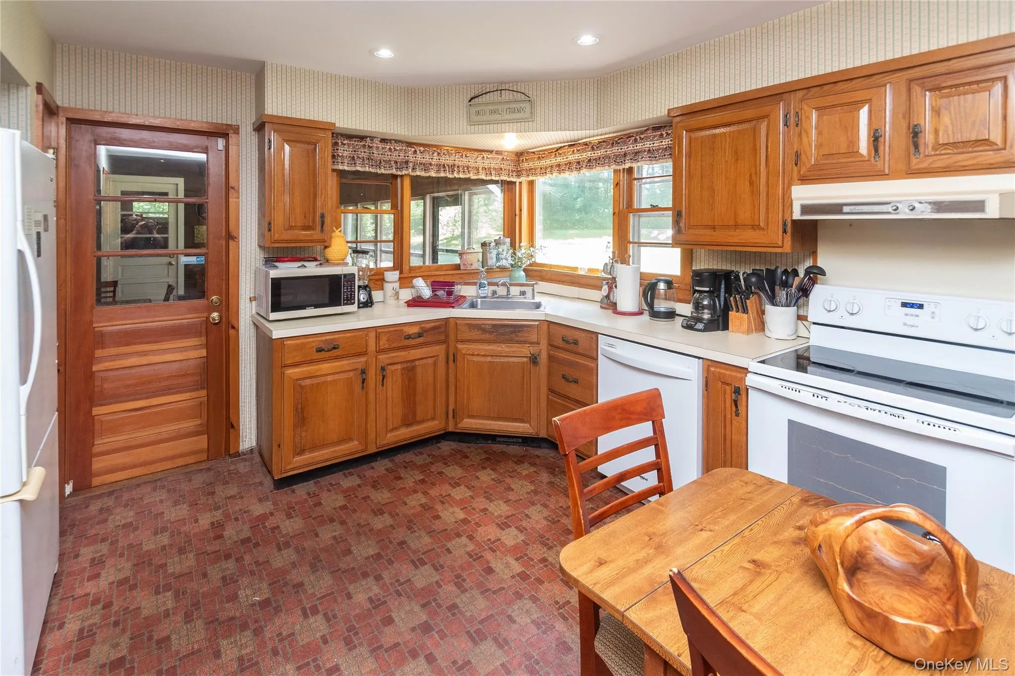 Kitchen featuring wallpapered walls, white appliances, light countertops, and brown cabinetry Kitchen featuring wallpapered walls, white appliances, light countertops, and brown cabinetry