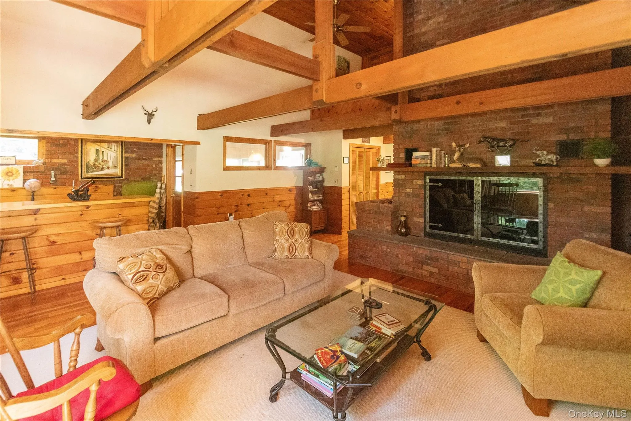 Living area featuring wooden walls, wood finished floors, a wainscoted wall, a fireplace, and a ceiling fan Living area featuring wooden walls, wood finished floors, a wainscoted wall, a fireplace, and a ceiling fan