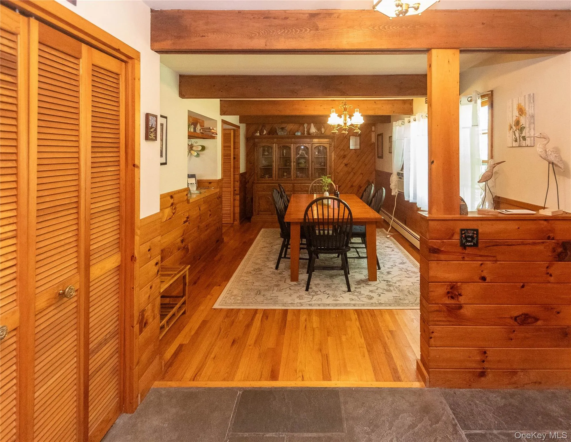 Dining space with wood walls, wood finished floors, beamed ceiling, baseboard heating, and a wainscoted wall Dining space with wood walls, wood finished floors, beamed ceiling, baseboard heating, and a wainscoted wall