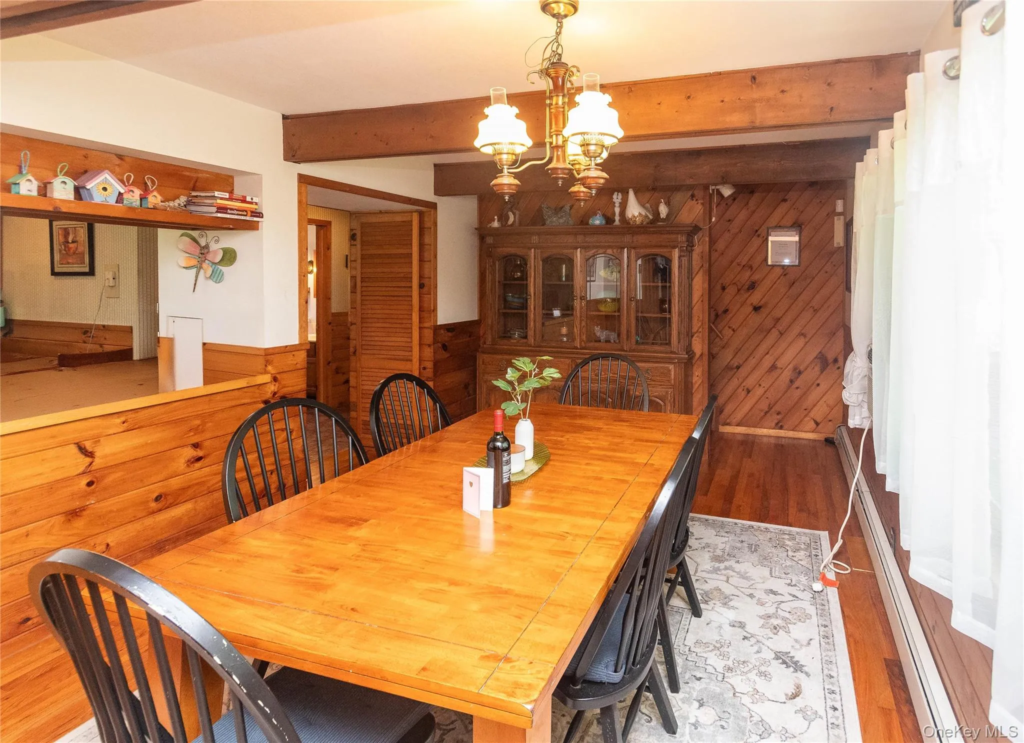 Dining space with wooden walls, a chandelier, light wood finished floors, a baseboard radiator, and beamed ceiling Dining space with wooden walls, a chandelier, light wood finished floors, a baseboard radiator, and beamed ceiling
