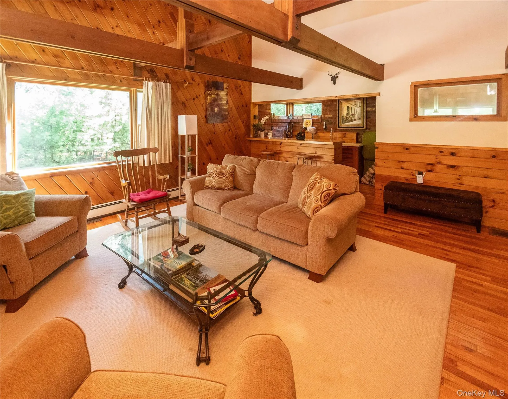 Living room with wood walls, beamed ceiling, wood finished floors, and baseboard heating Living room with wood walls, beamed ceiling, wood finished floors, and baseboard heating