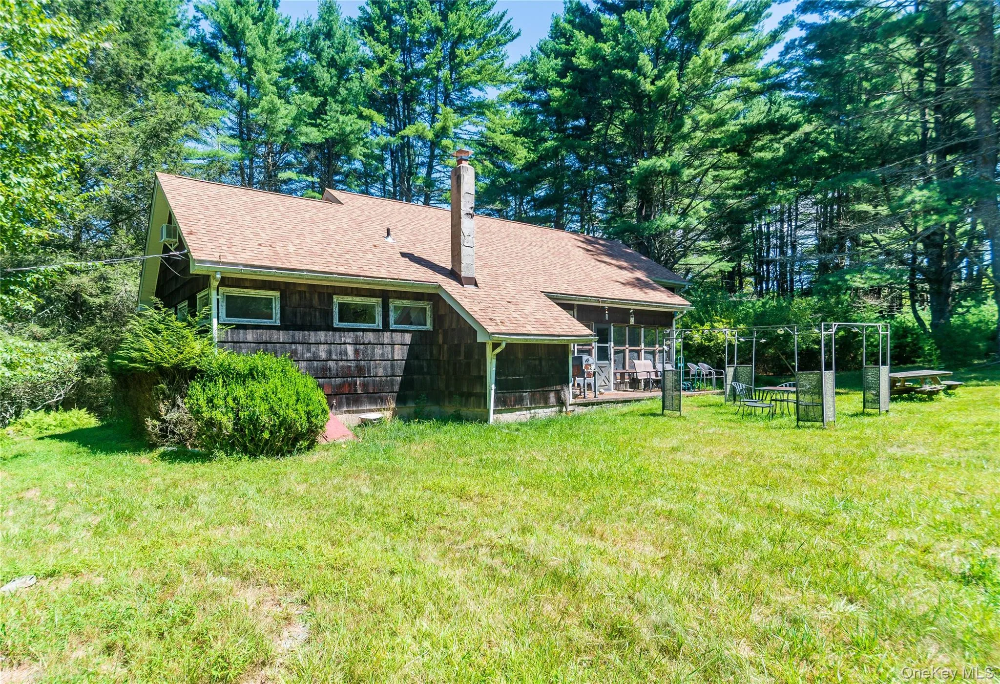 Rear view of property featuring a chimney, view of scattered trees, a shingled roof, and a lawn Rear view of property featuring a chimney, view of scattered trees, a shingled roof, and a lawn