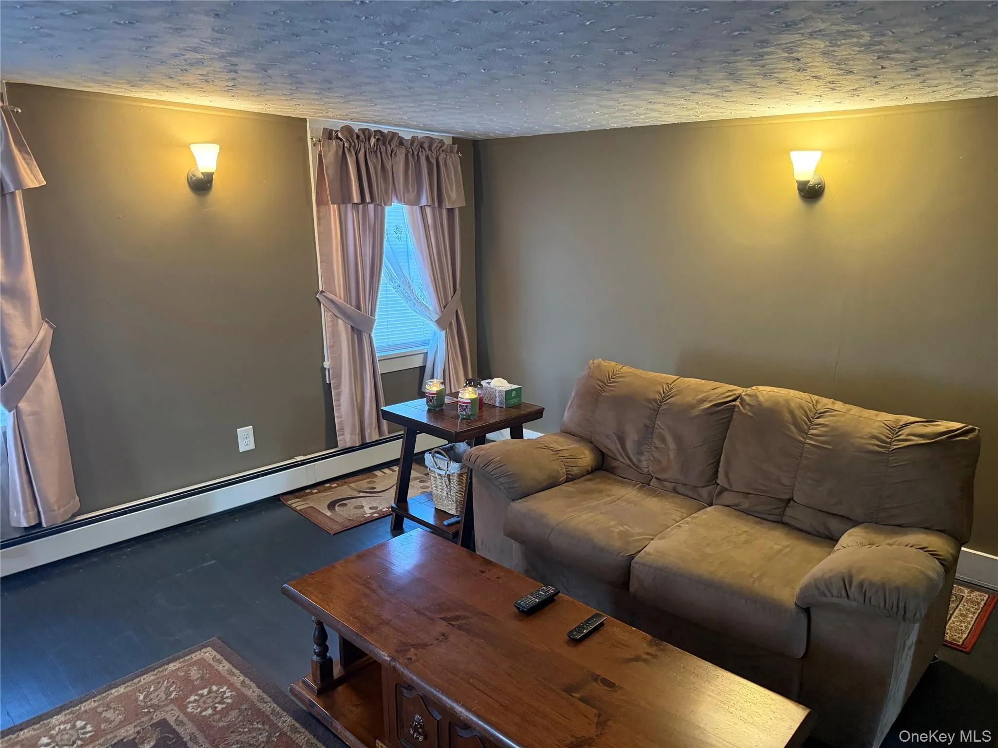 Living area with a baseboard radiator, a textured ceiling, and wood finished floors Living area with a baseboard radiator, a textured ceiling, and wood finished floors