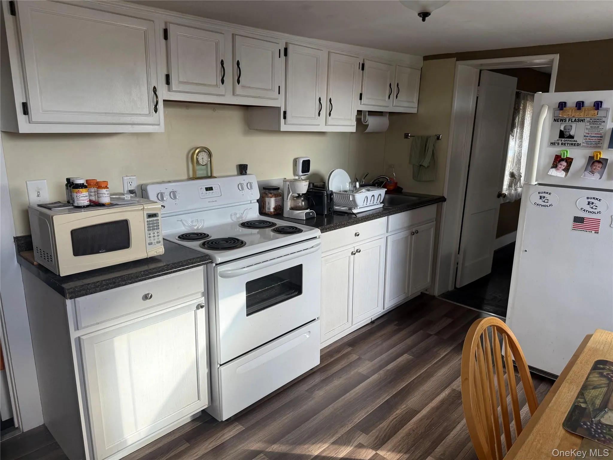 Kitchen featuring dark countertops, white appliances, white cabinetry, and dark wood-style floors Kitchen featuring dark countertops, white appliances, white cabinetry, and dark wood-style floors