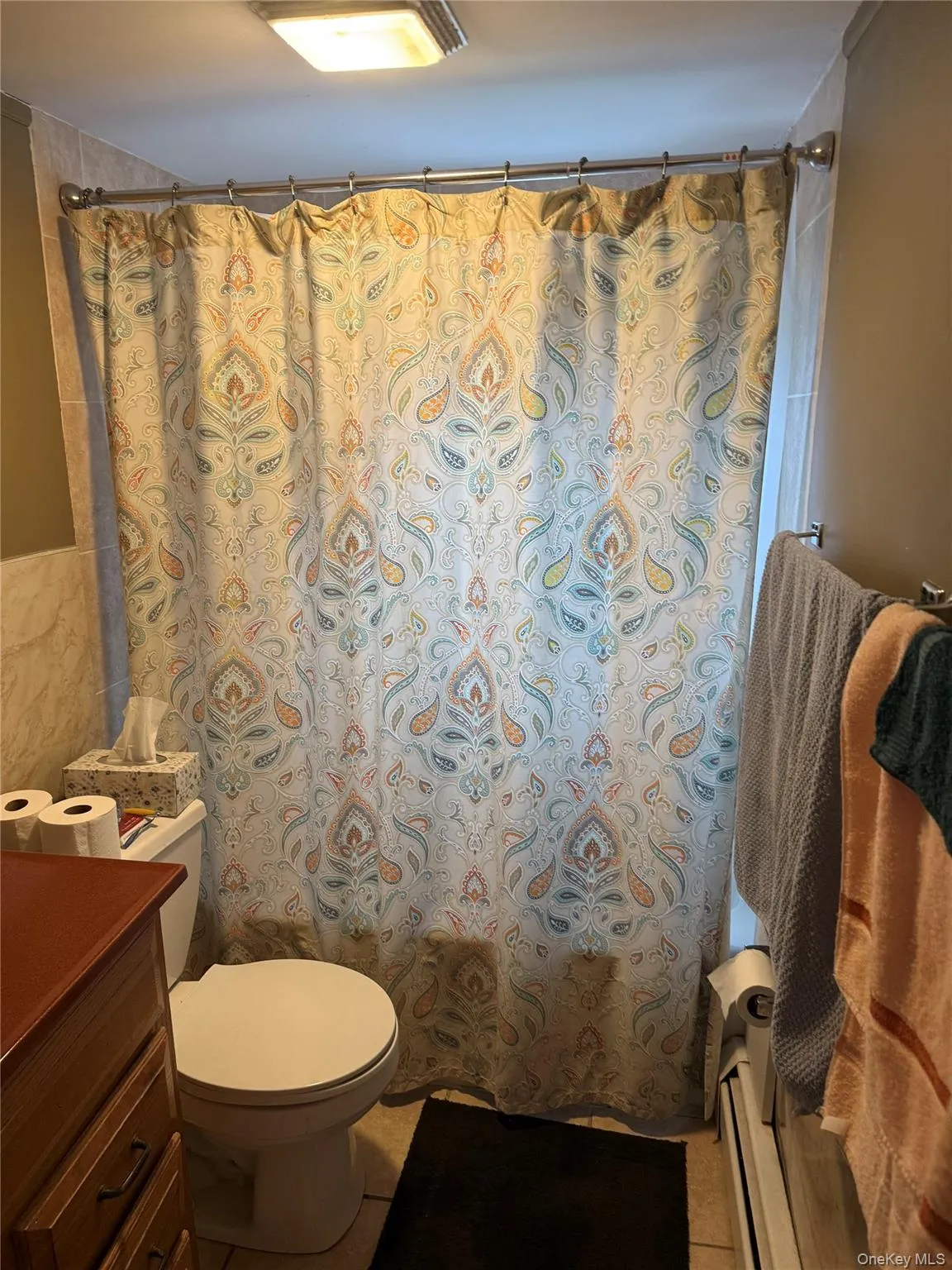 Bathroom featuring vanity, tile walls, a baseboard heating unit, shower / tub combo with curtain, and light tile patterned floors Bathroom featuring vanity, tile walls, a baseboard heating unit, shower / tub combo with curtain, and light tile patterned floors