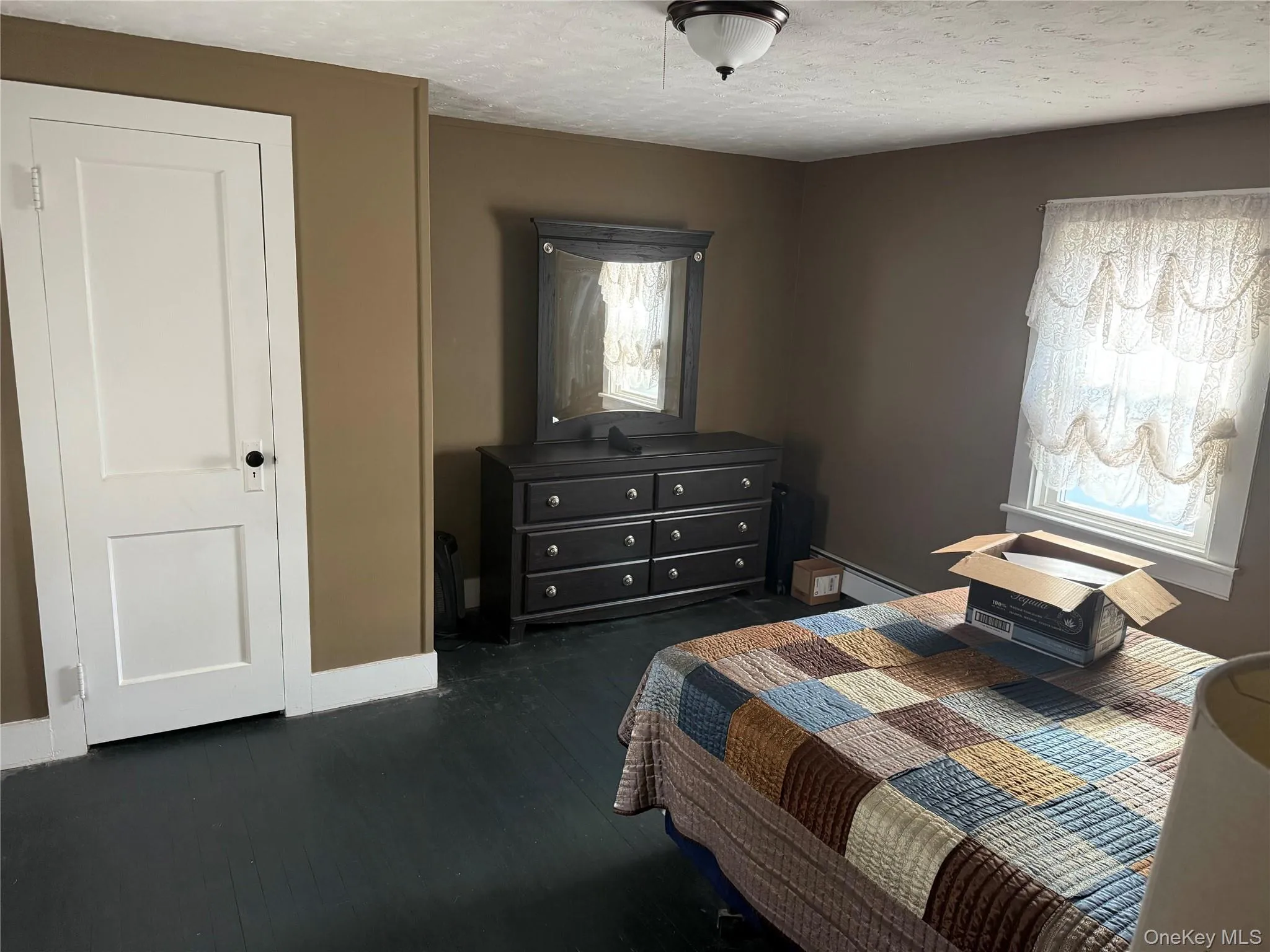 Bedroom with a textured ceiling, dark wood-style floors, and a baseboard radiator Bedroom with a textured ceiling, dark wood-style floors, and a baseboard radiator