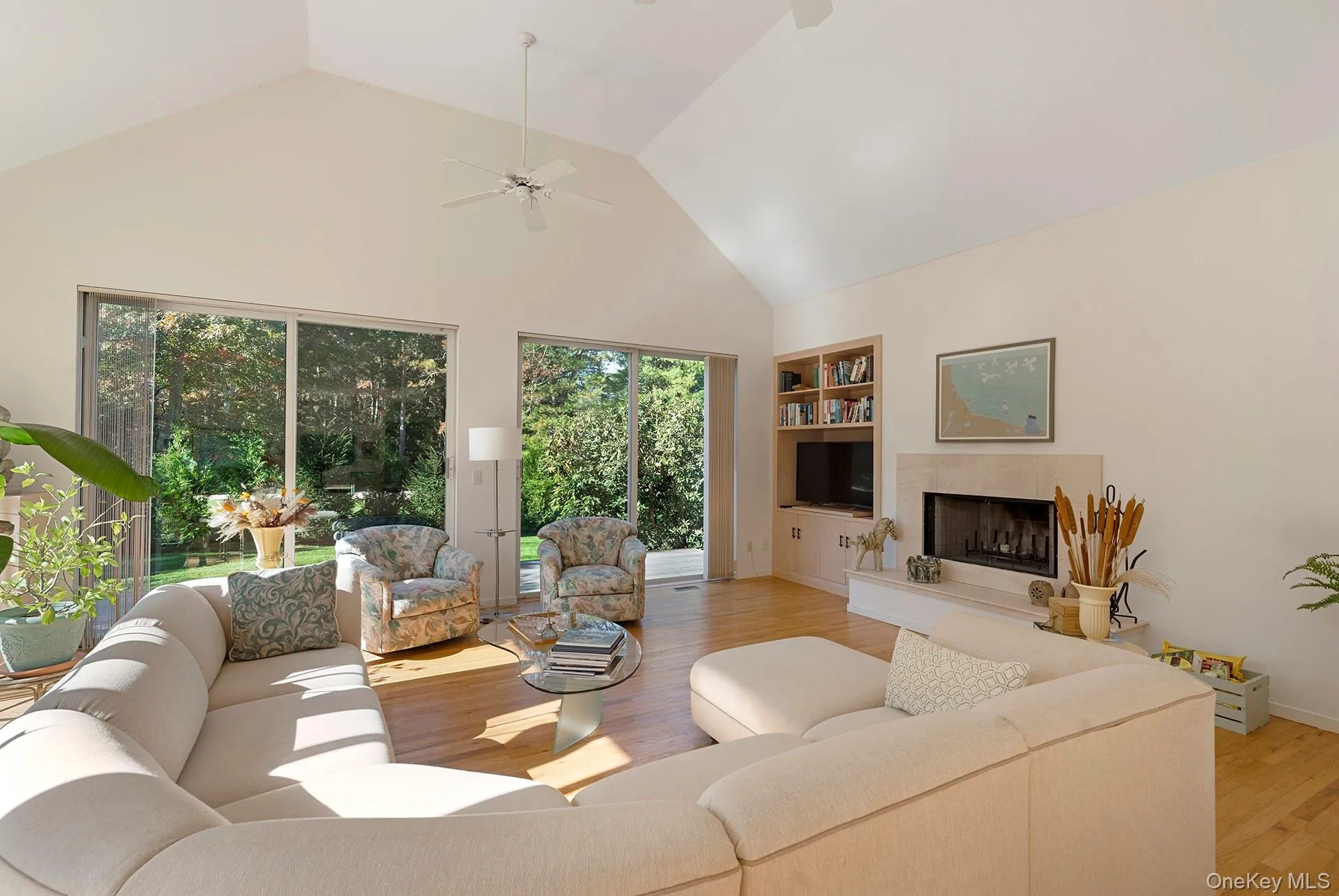 Living area featuring high vaulted ceiling, a tiled fireplace, light wood finished floors, built in features, and ceiling fan Living area featuring high vaulted ceiling, a tiled fireplace, light wood finished floors, built in features, and ceiling fan