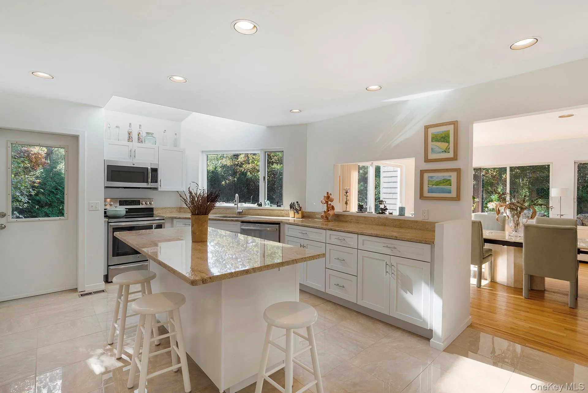 Kitchen featuring recessed lighting, stainless steel appliances, a breakfast bar, white cabinetry, and light stone counters Kitchen featuring recessed lighting, stainless steel appliances, a breakfast bar, white cabinetry, and light stone counters