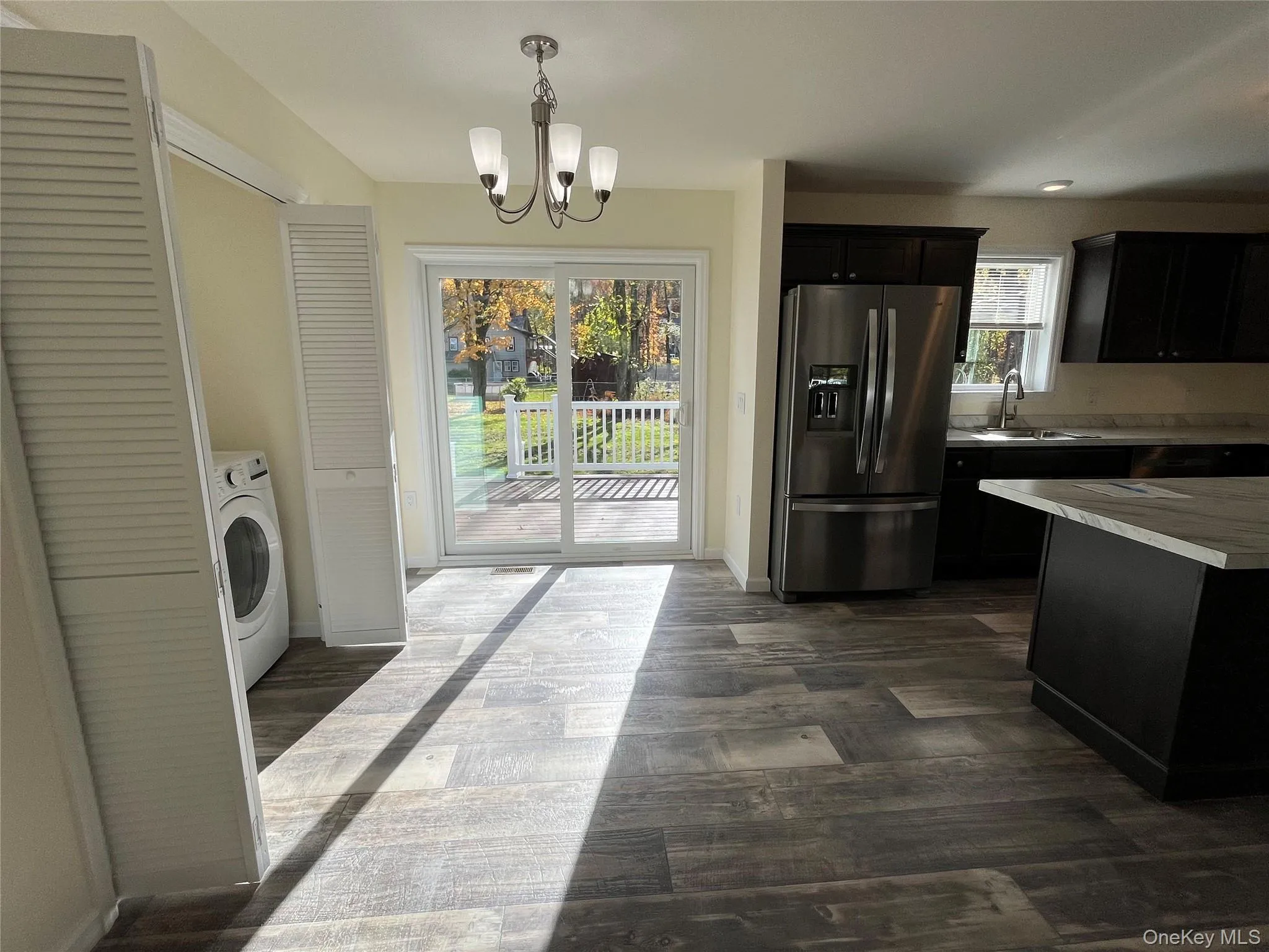 Kitchen featuring light countertops, stainless steel fridge, dark cabinets, hanging light fixtures, and dark wood-style flooring Kitchen featuring light countertops, stainless steel fridge, dark cabinets, hanging light fixtures, and dark wood-style flooring