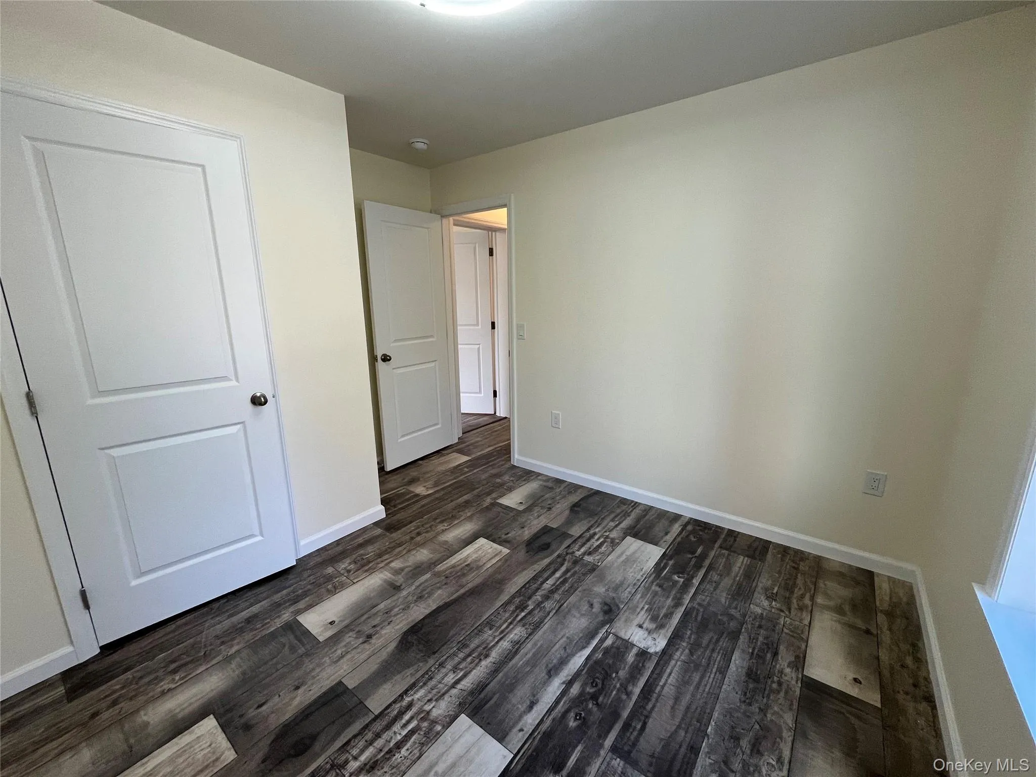 Unfurnished bedroom with dark wood finished floors and baseboards Unfurnished bedroom with dark wood finished floors and baseboards