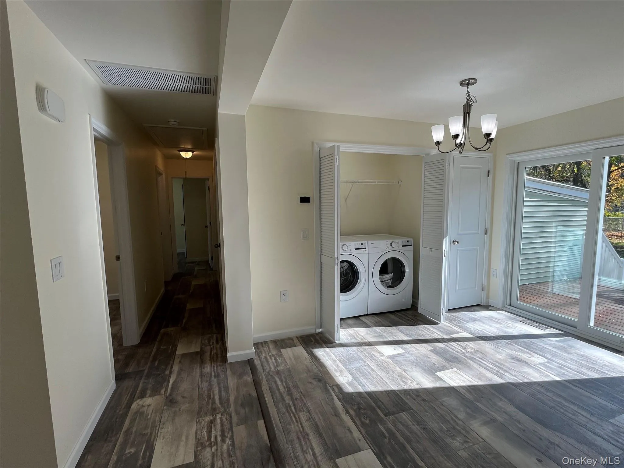 Laundry area featuring dark wood finished floors, washing machine and clothes dryer, and a chandelier Laundry area featuring dark wood finished floors, washing machine and clothes dryer, and a chandelier