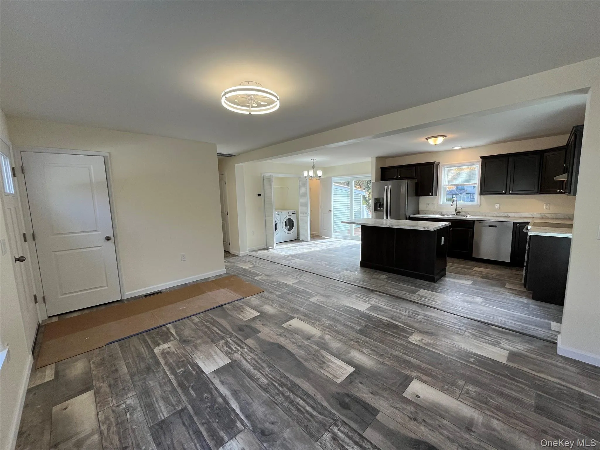 Kitchen featuring a kitchen island, stainless steel appliances, dark wood-style floors, a chandelier, and dark cabinetry Kitchen featuring a kitchen island, stainless steel appliances, dark wood-style floors, a chandelier, and dark cabinetry