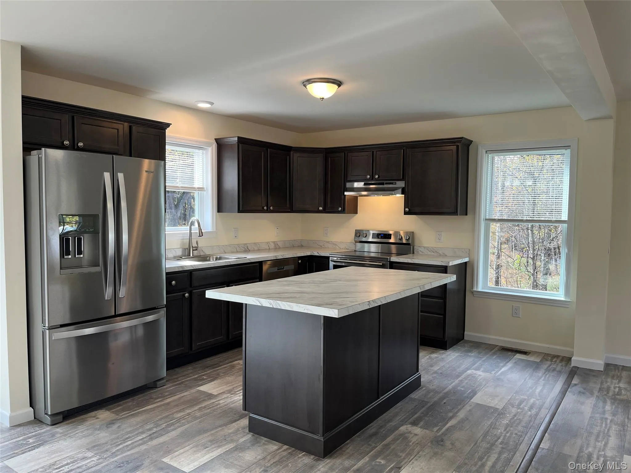 Kitchen featuring stainless steel appliances, light countertops, dark wood-style flooring, and dark brown cabinetry Kitchen featuring stainless steel appliances, light countertops, dark wood-style flooring, and dark brown cabinetry
