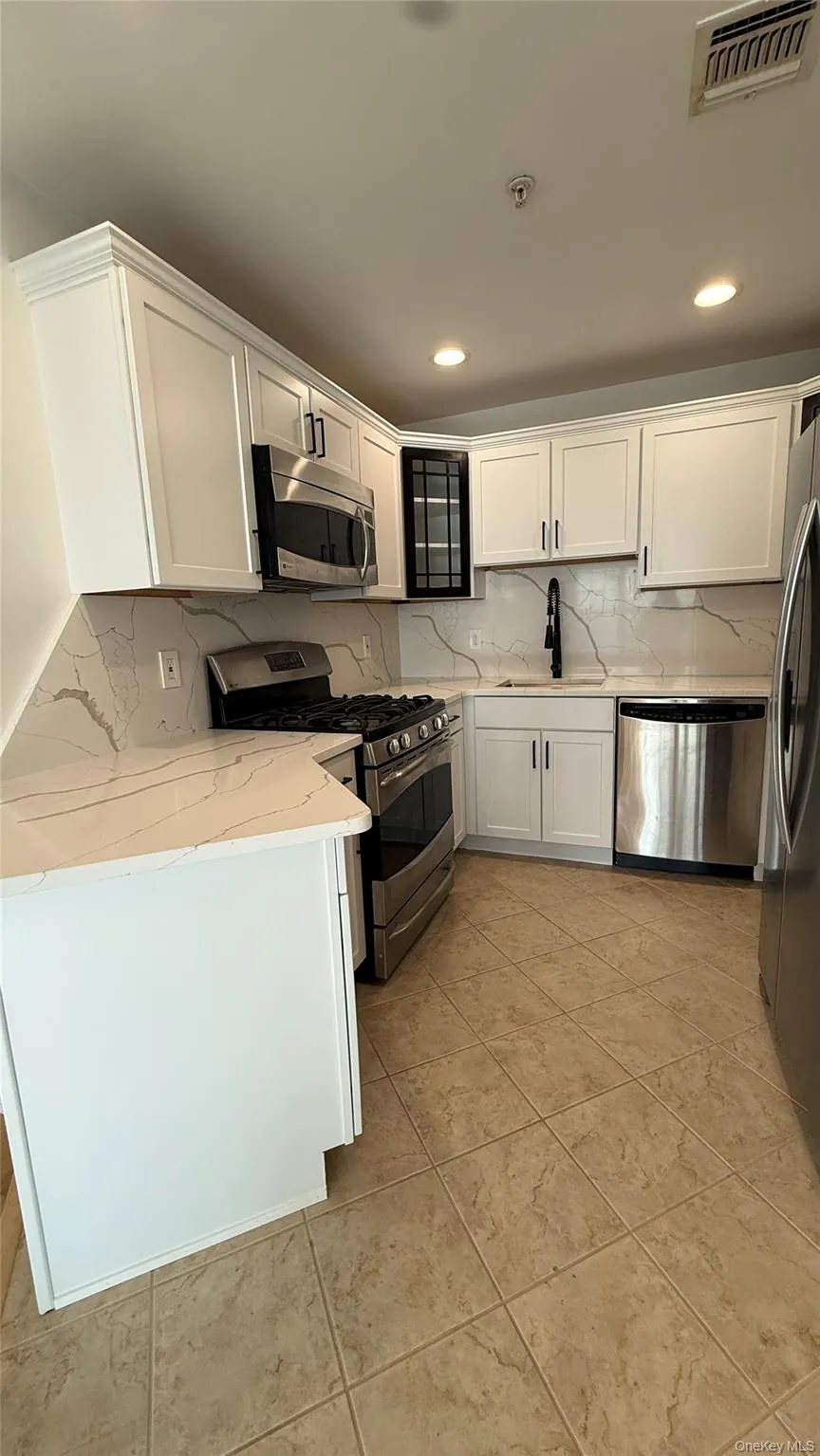 Kitchen with white cabinets, appliances with stainless steel finishes, backsplash, light stone counters, and glass insert cabinets Kitchen with white cabinets, appliances with stainless steel finishes, backsplash, light stone counters, and glass insert cabinets