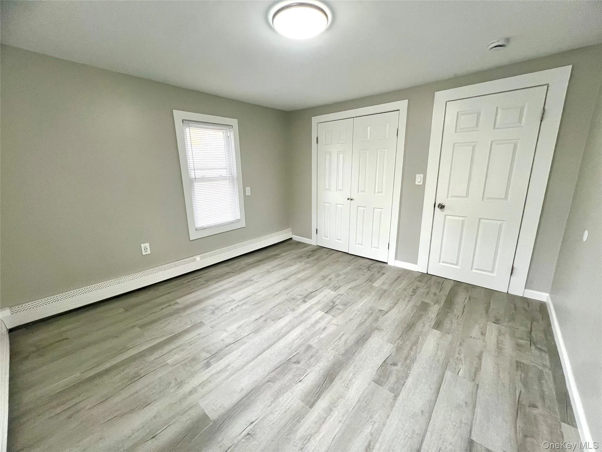 Unfurnished bedroom featuring a baseboard heating unit, light wood-type flooring, and a closet Unfurnished bedroom featuring a baseboard heating unit, light wood-type flooring, and a closet
