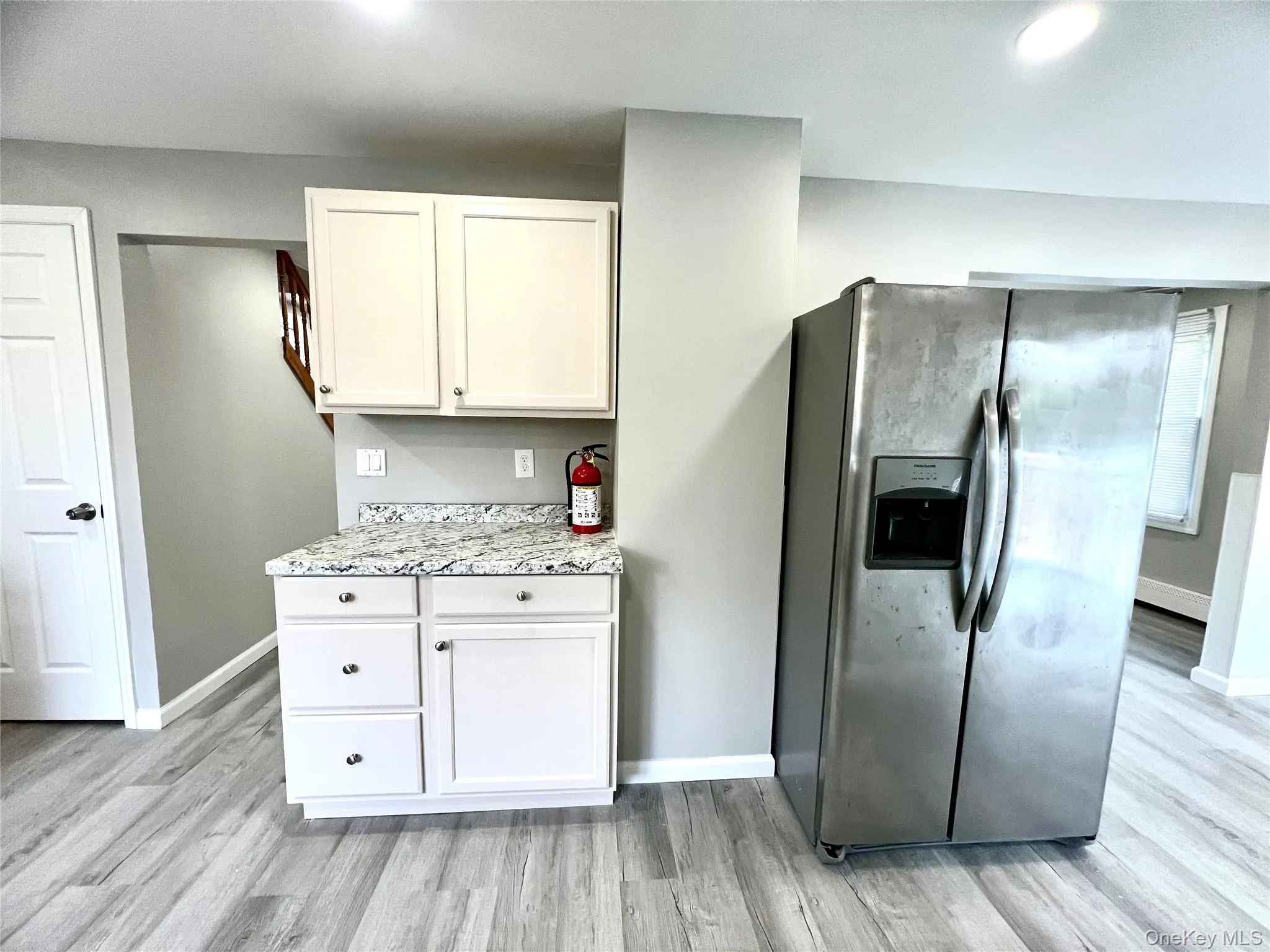 Kitchen with stainless steel fridge with ice dispenser, white cabinets, light wood finished floors, light stone countertops, and recessed lighting Kitchen with stainless steel fridge with ice dispenser, white cabinets, light wood finished floors, light stone countertops, and recessed lighting
