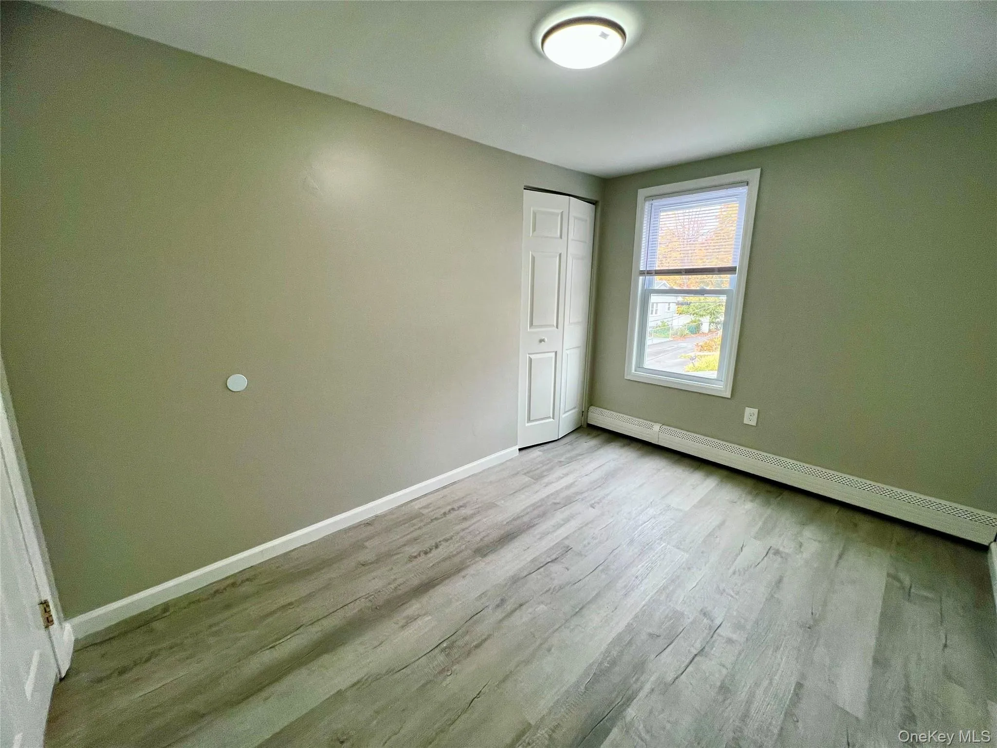 Unfurnished bedroom with a baseboard heating unit, light wood-style floors, and a closet Unfurnished bedroom with a baseboard heating unit, light wood-style floors, and a closet