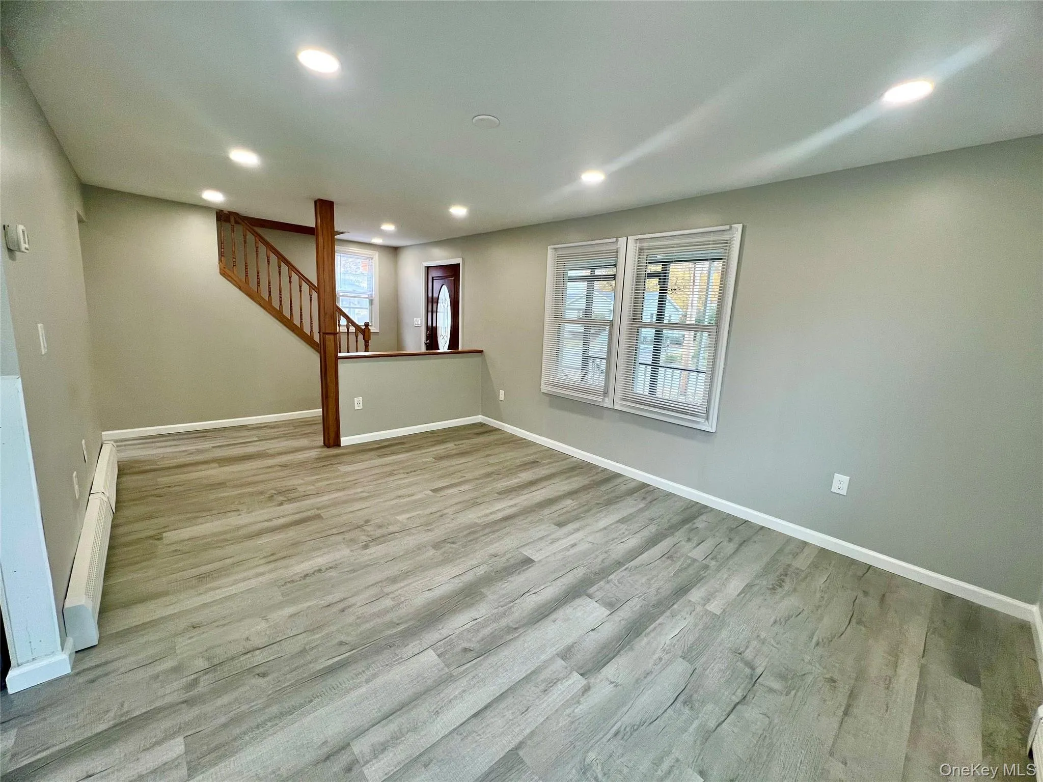 Unfurnished living room featuring recessed lighting, light wood finished floors, stairway, and a baseboard radiator Unfurnished living room featuring recessed lighting, light wood finished floors, stairway, and a baseboard radiator