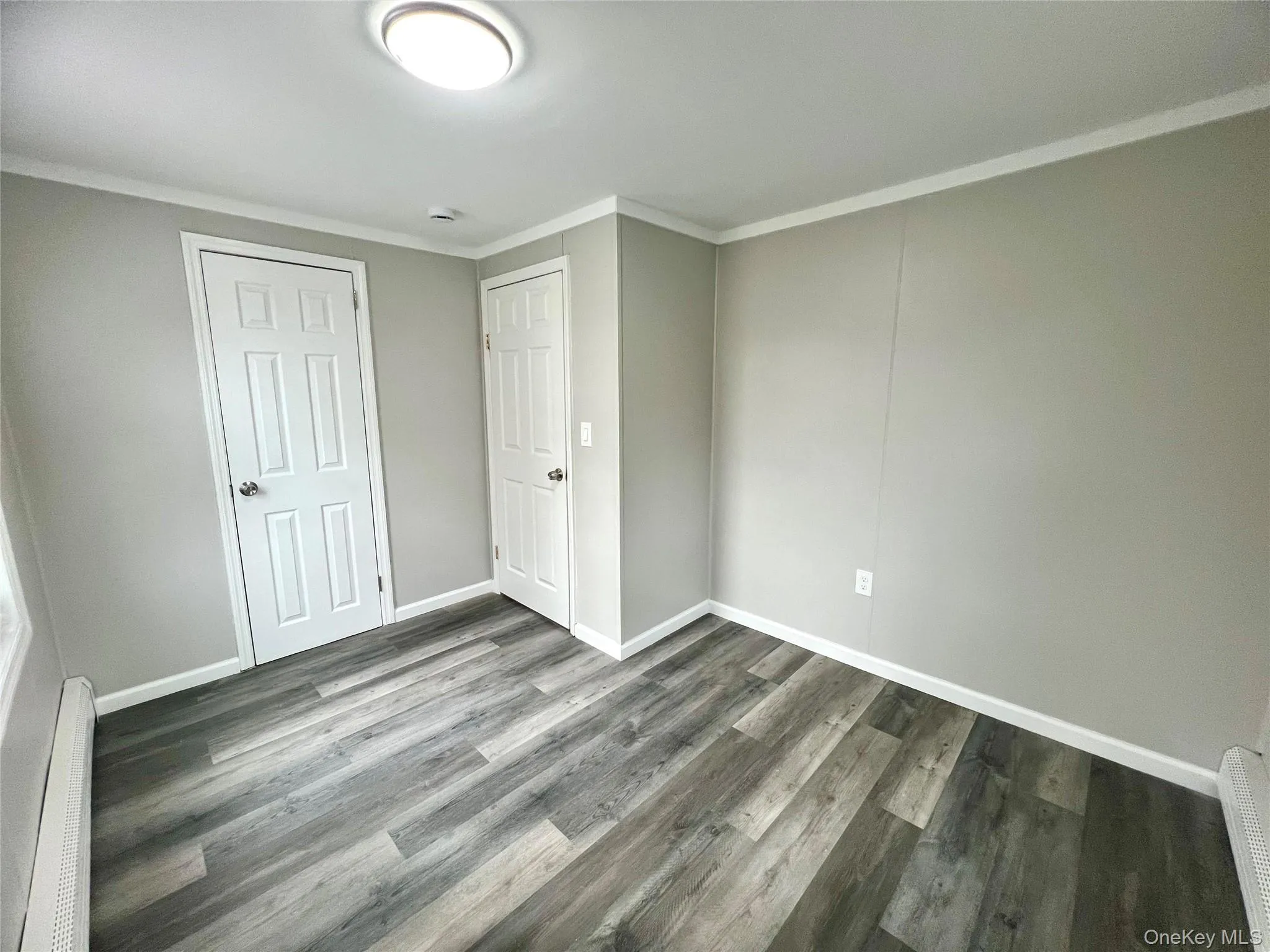 Unfurnished bedroom featuring crown molding, baseboard heating, wood finished floors, and a closet Unfurnished bedroom featuring crown molding, baseboard heating, wood finished floors, and a closet