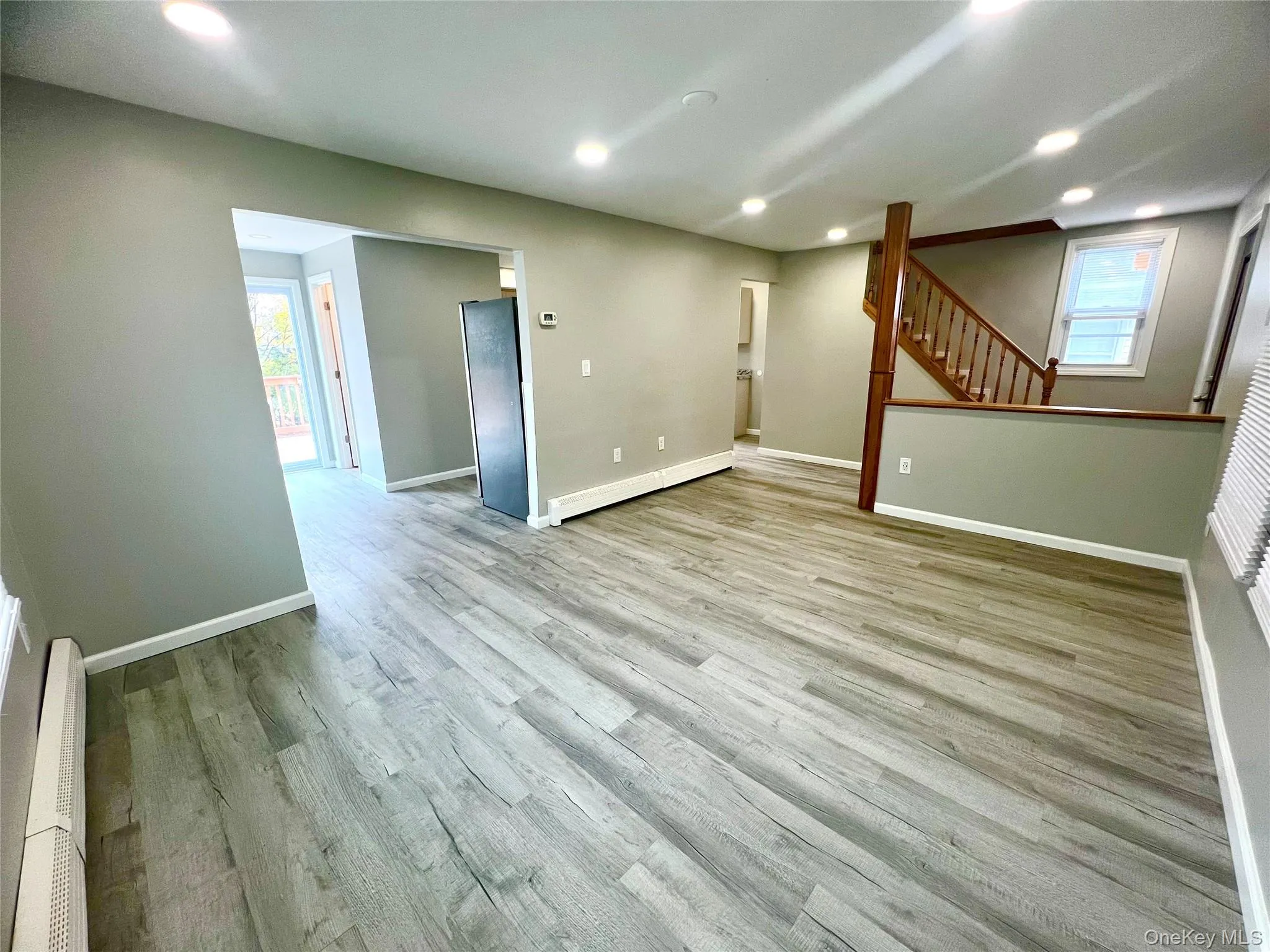Below grade area with recessed lighting, light wood-style floors, baseboard heating, freestanding refrigerator, and stairs Below grade area with recessed lighting, light wood-style floors, baseboard heating, freestanding refrigerator, and stairs