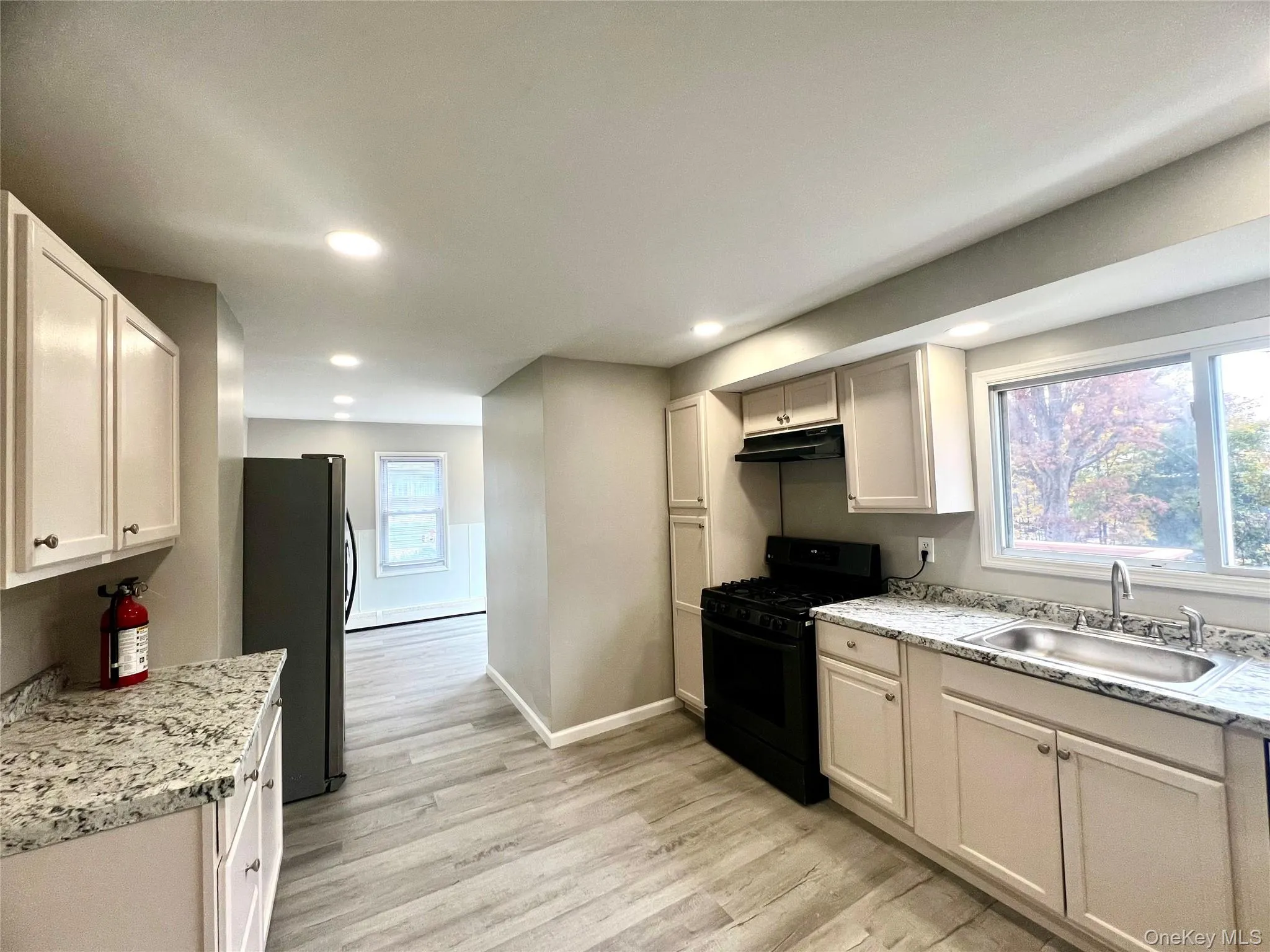 Kitchen with black range with gas stovetop, light wood-type flooring, freestanding refrigerator, light stone counters, and recessed lighting Kitchen with black range with gas stovetop, light wood-type flooring, freestanding refrigerator, light stone counters, and recessed lighting