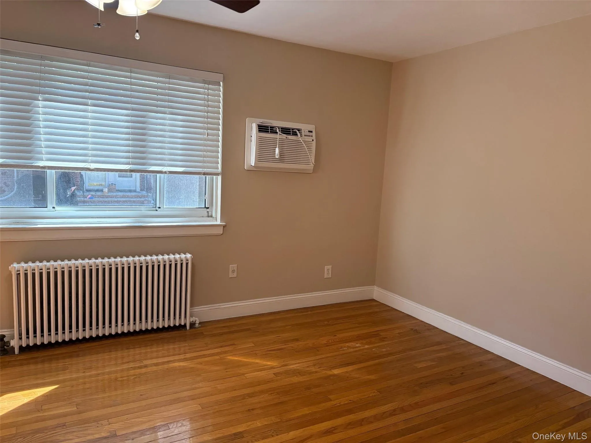 Unfurnished room with radiator, light wood-style flooring, ceiling fan, and a wall unit AC Unfurnished room with radiator, light wood-style flooring, ceiling fan, and a wall unit AC