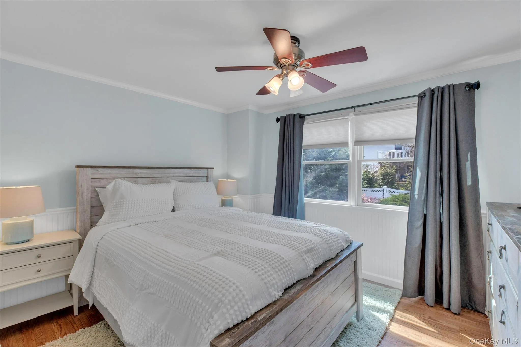 Bedroom with wainscoting, crown molding, light wood-style floors, and a ceiling fan Bedroom with wainscoting, crown molding, light wood-style floors, and a ceiling fan