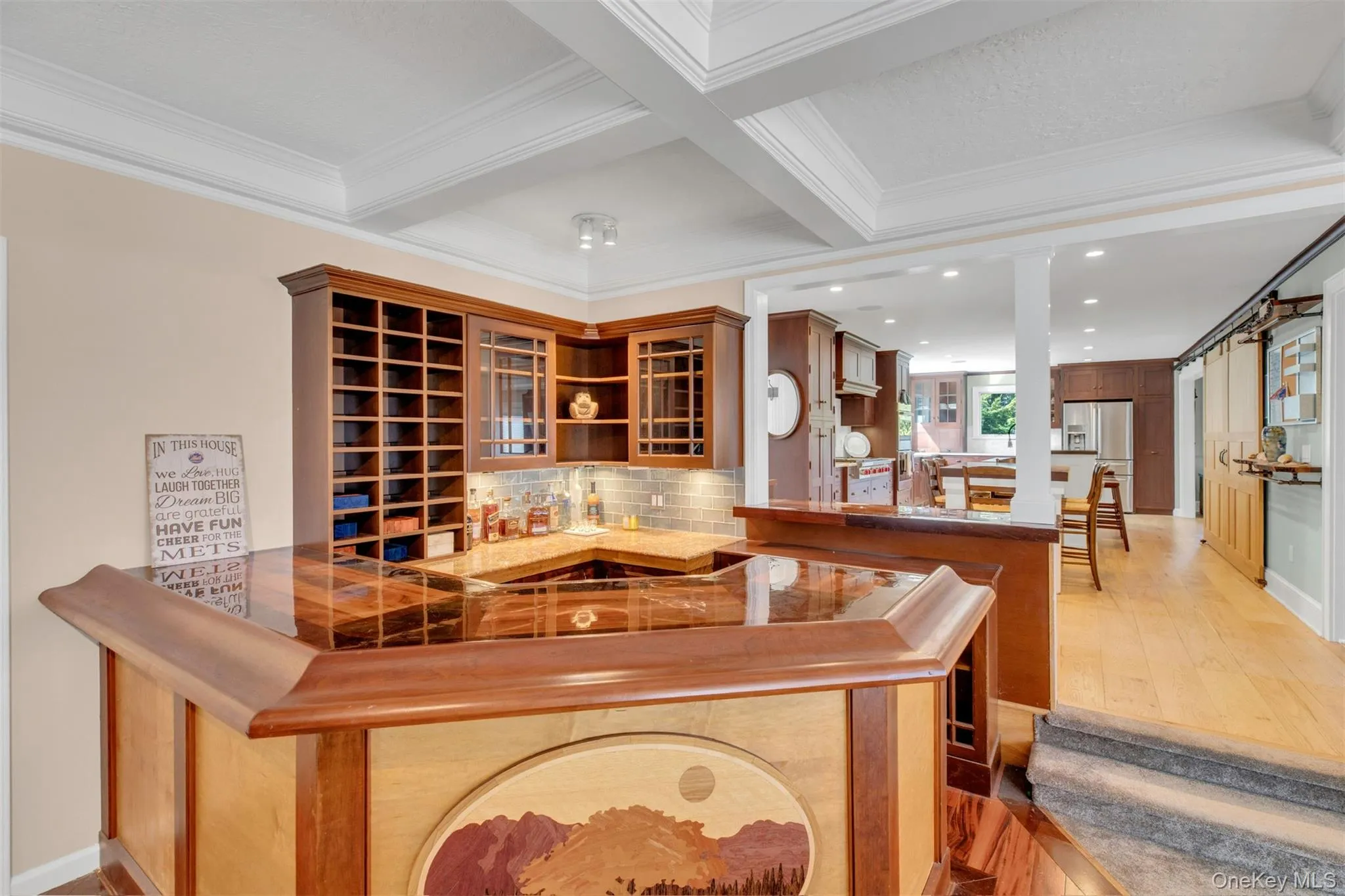Indoor wet bar with tasteful backsplash, brown cabinets, coffered ceiling, beamed ceiling, and stainless steel fridge Indoor wet bar with tasteful backsplash, brown cabinets, coffered ceiling, beamed ceiling, and stainless steel fridge