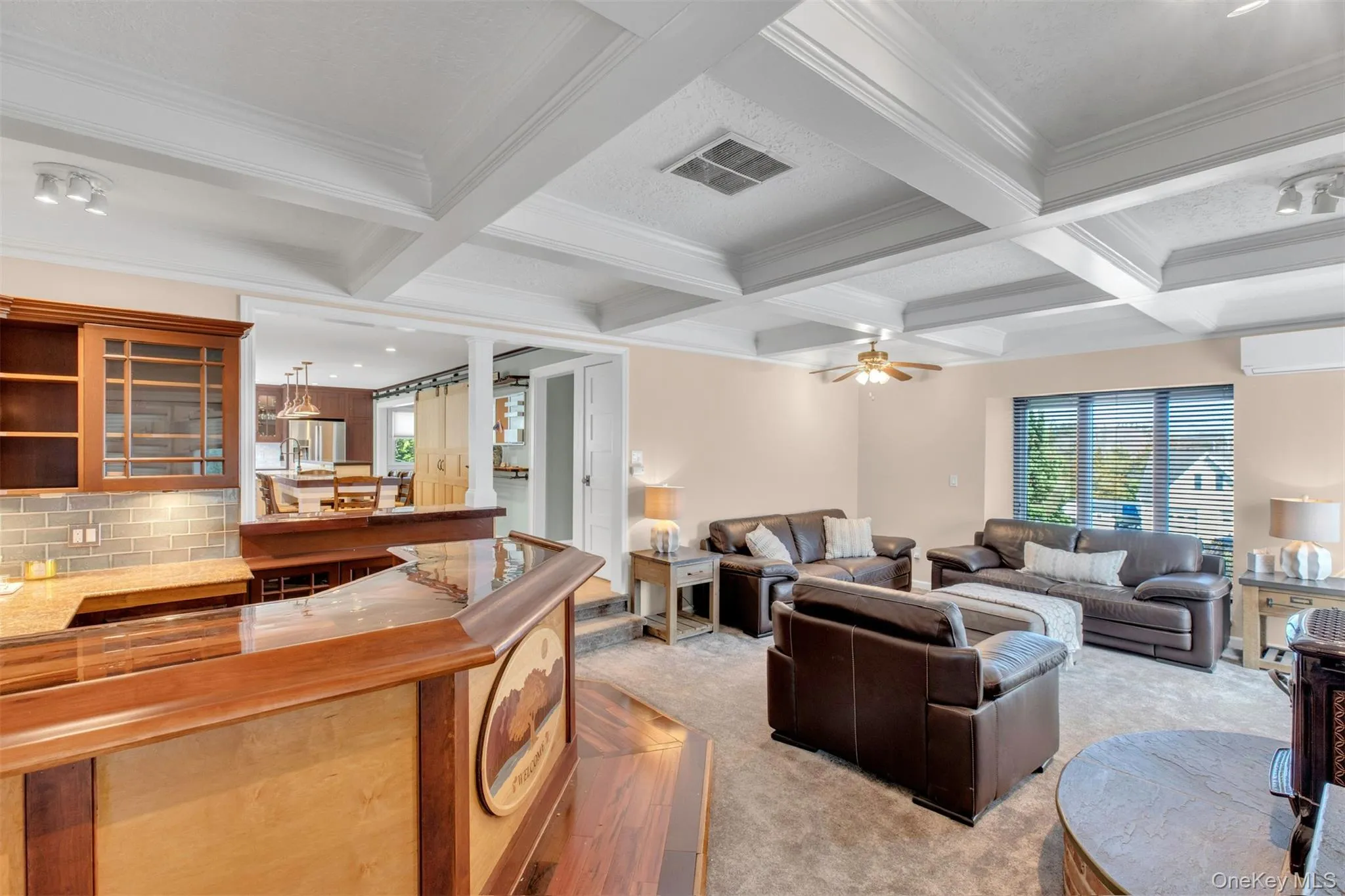 Living room featuring beam ceiling, coffered ceiling, ornamental molding, light carpet, and an AC wall unit Living room featuring beam ceiling, coffered ceiling, ornamental molding, light carpet, and an AC wall unit