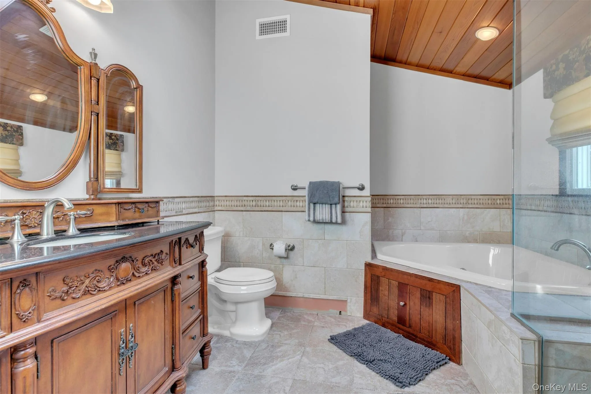 Full bath featuring vanity, a bath, tile walls, a wainscoted wall, and wooden ceiling Full bath featuring vanity, a bath, tile walls, a wainscoted wall, and wooden ceiling