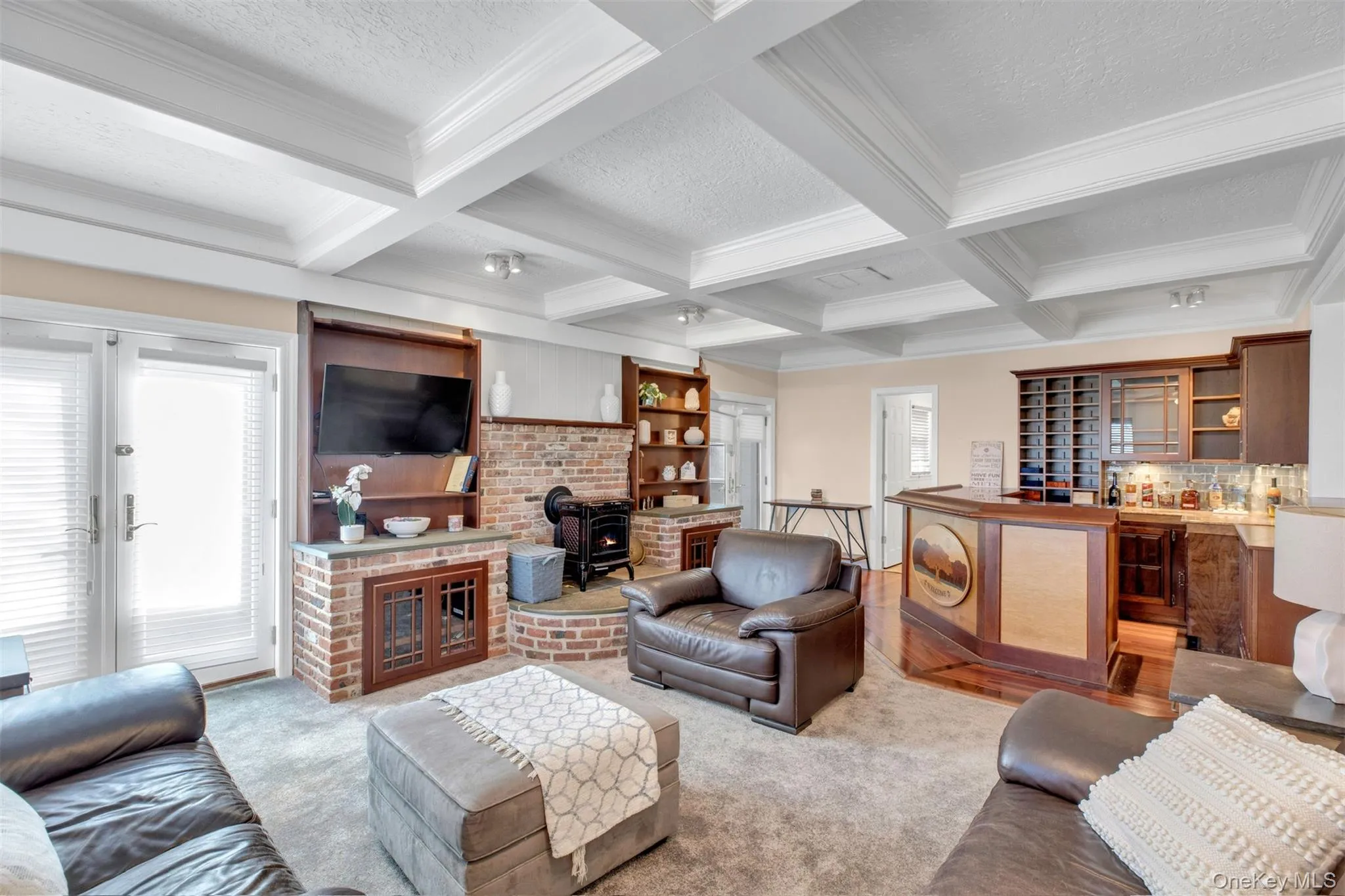Carpeted living room featuring a wood stove, beamed ceiling, coffered ceiling, crown molding, and a textured ceiling Carpeted living room featuring a wood stove, beamed ceiling, coffered ceiling, crown molding, and a textured ceiling