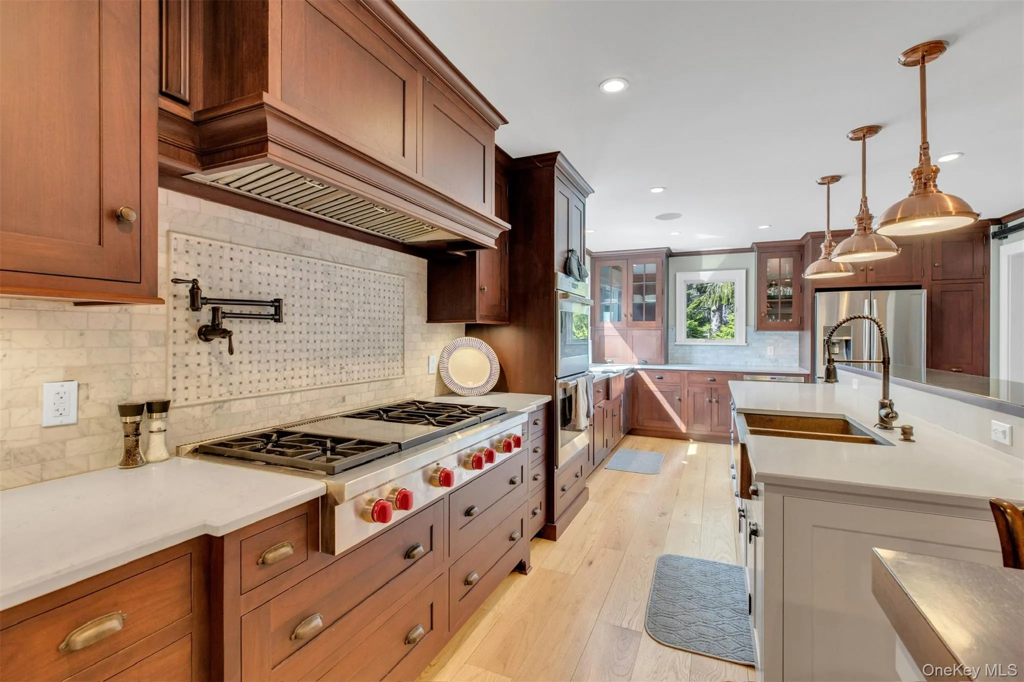 Kitchen featuring tasteful backsplash, light stone counters, appliances with stainless steel finishes, hanging light fixtures, and light wood-type flooring Kitchen featuring tasteful backsplash, light stone counters, appliances with stainless steel finishes, hanging light fixtures, and light wood-type flooring