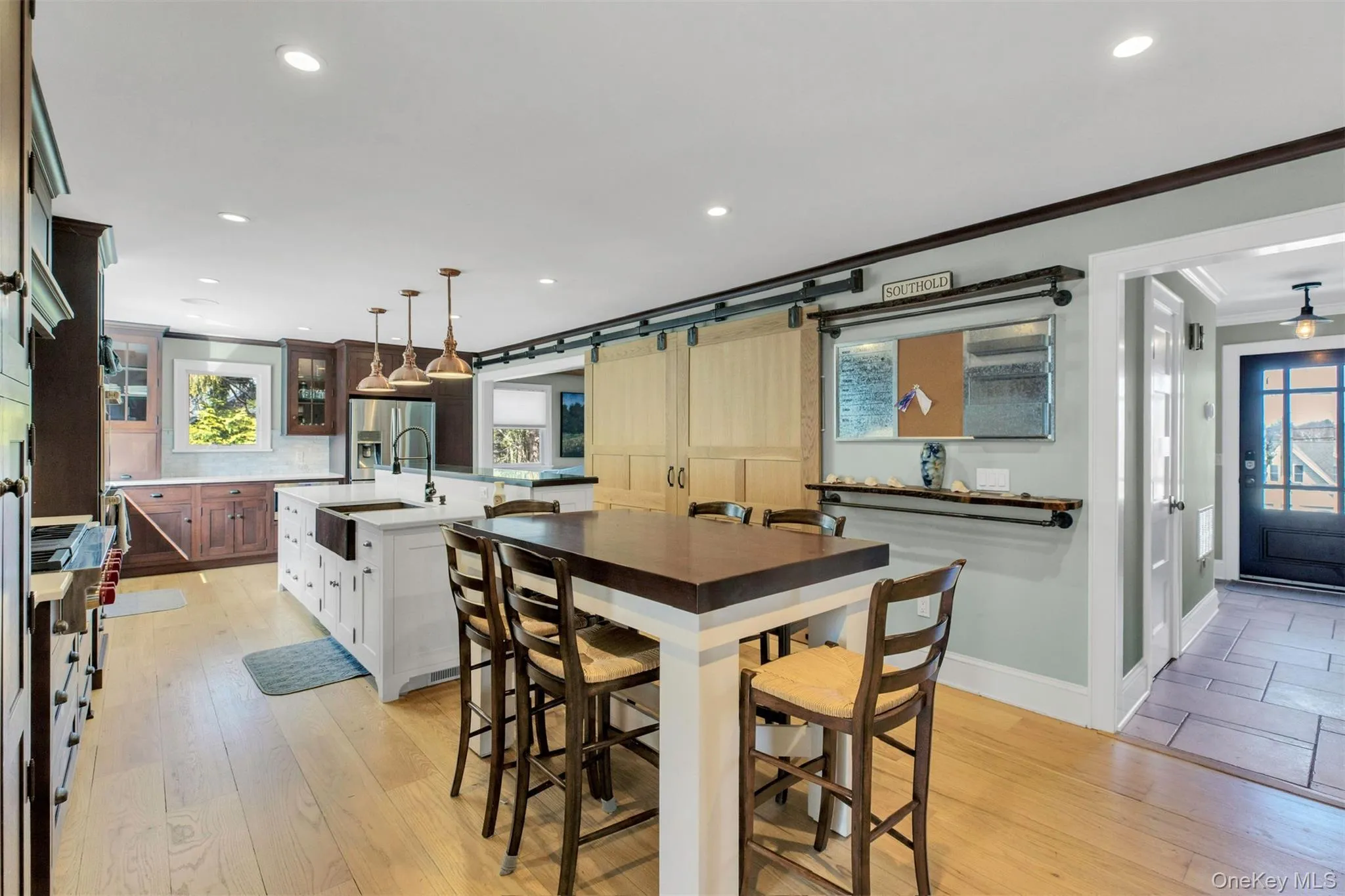 Kitchen featuring white cabinets, glass insert cabinets, a center island with sink, decorative light fixtures, and light wood-style floors Kitchen featuring white cabinets, glass insert cabinets, a center island with sink, decorative light fixtures, and light wood-style floors