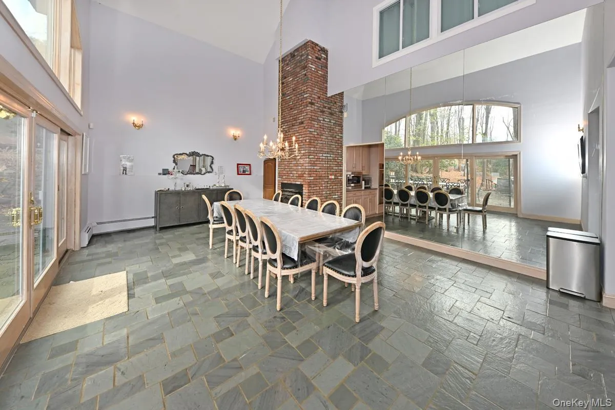Dining space featuring stone tile floors, high vaulted ceiling, a chandelier, a baseboard heating unit, and a brick fireplace Dining space featuring stone tile floors, high vaulted ceiling, a chandelier, a baseboard heating unit, and a brick fireplace