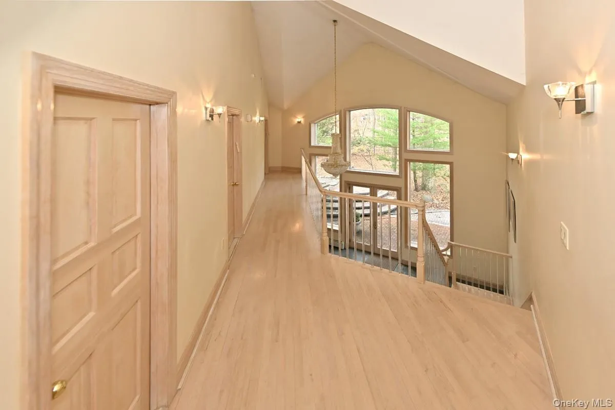 Corridor with high vaulted ceiling, an upstairs landing, and light wood-type flooring Corridor with high vaulted ceiling, an upstairs landing, and light wood-type flooring