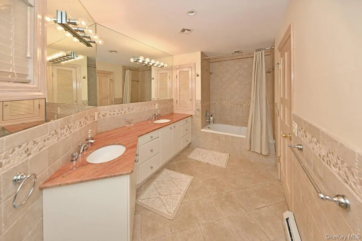 Full bathroom featuring double vanity, tile walls, tiled shower / bath, a baseboard heating unit, and tasteful backsplash Full bathroom featuring double vanity, tile walls, tiled shower / bath, a baseboard heating unit, and tasteful backsplash