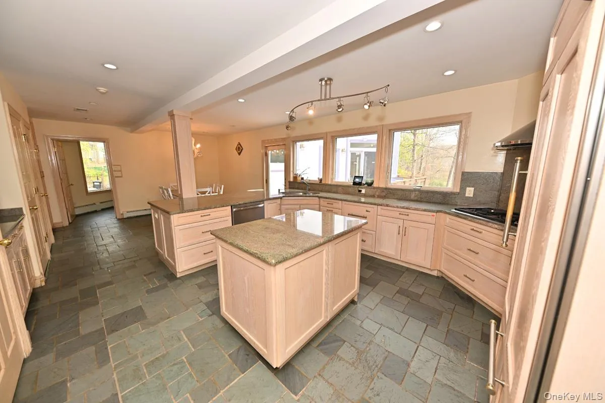 Kitchen featuring light brown cabinetry, a peninsula, a center island, backsplash, and stone tile floors Kitchen featuring light brown cabinetry, a peninsula, a center island, backsplash, and stone tile floors