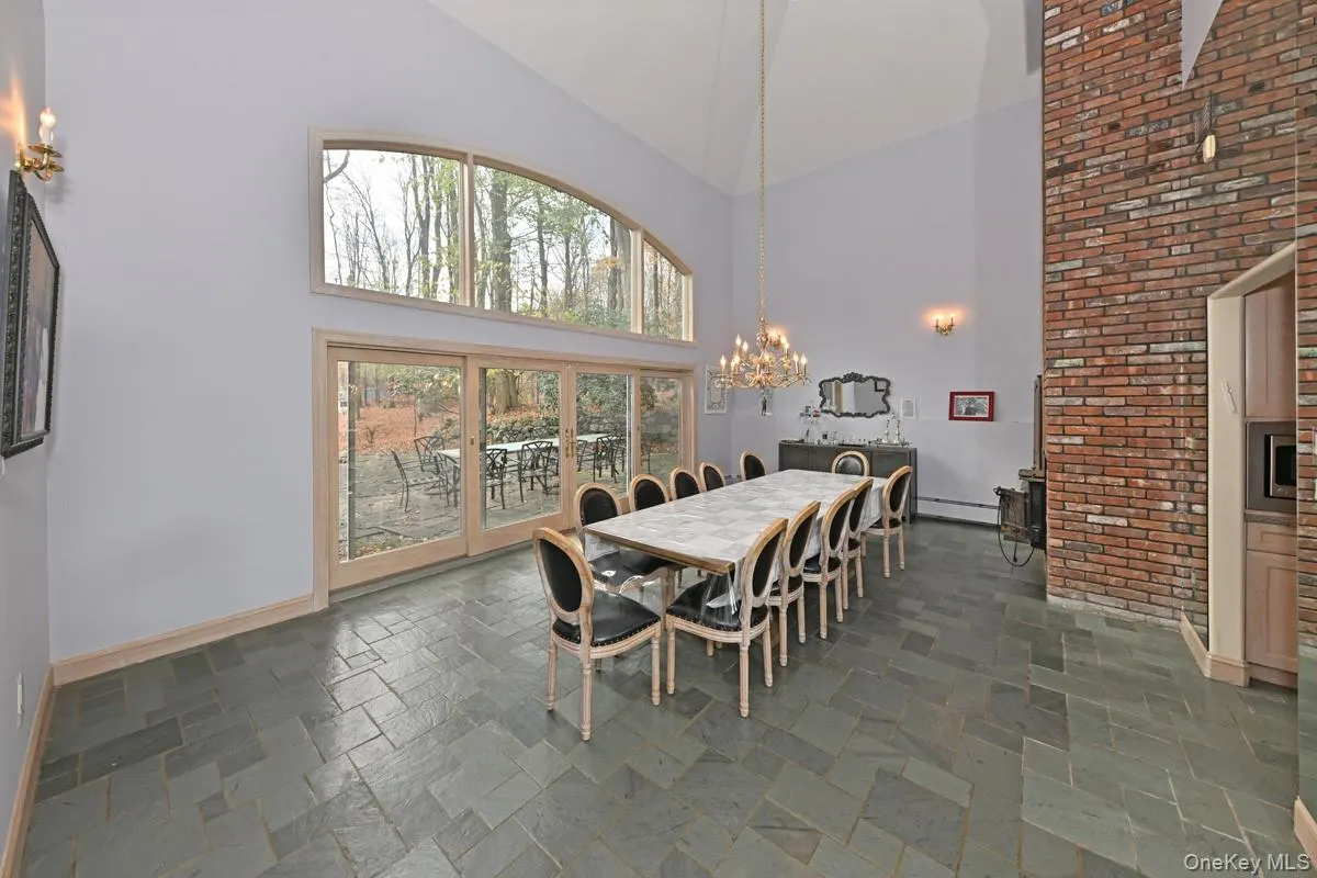 Dining area featuring high vaulted ceiling, stone tile flooring, a chandelier, a baseboard radiator, and brick wall Dining area featuring high vaulted ceiling, stone tile flooring, a chandelier, a baseboard radiator, and brick wall