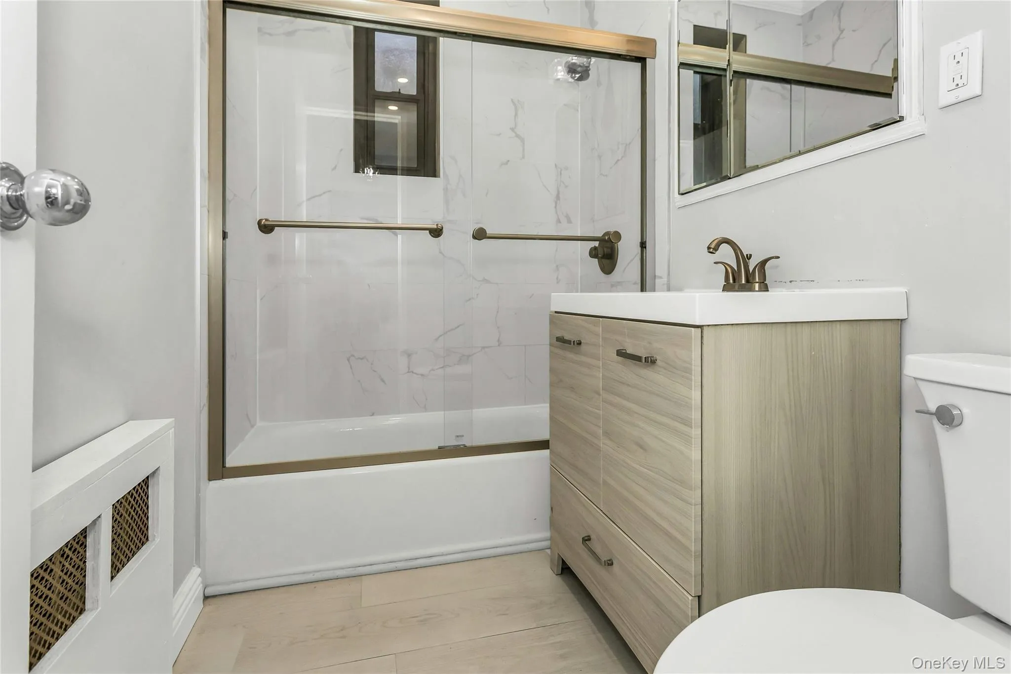 Bathroom with vanity, shower / bath combination with glass door, and radiator heating unit Bathroom with vanity, shower / bath combination with glass door, and radiator heating unit