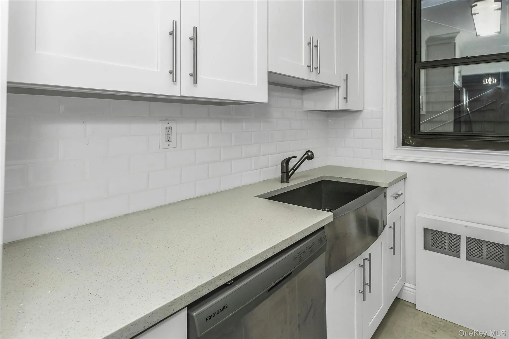 Kitchen featuring radiator, white cabinetry, stainless steel dishwasher, light stone counters, and decorative backsplash Kitchen featuring radiator, white cabinetry, stainless steel dishwasher, light stone counters, and decorative backsplash