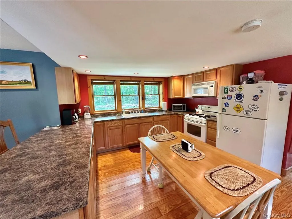 Kitchen with white appliances, light wood finished floors, brown cabinetry, and recessed lighting Kitchen with white appliances, light wood finished floors, brown cabinetry, and recessed lighting