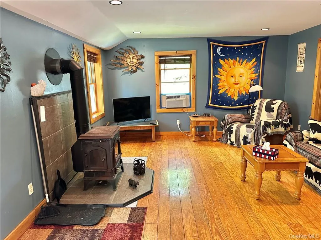Living area with a wood stove, light wood finished floors, recessed lighting, and vaulted ceiling Living area with a wood stove, light wood finished floors, recessed lighting, and vaulted ceiling