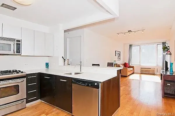 Kitchen with dark cabinetry, stainless steel appliances, light wood finished floors, white cabinetry, and a peninsula Kitchen with dark cabinetry, stainless steel appliances, light wood finished floors, white cabinetry, and a peninsula