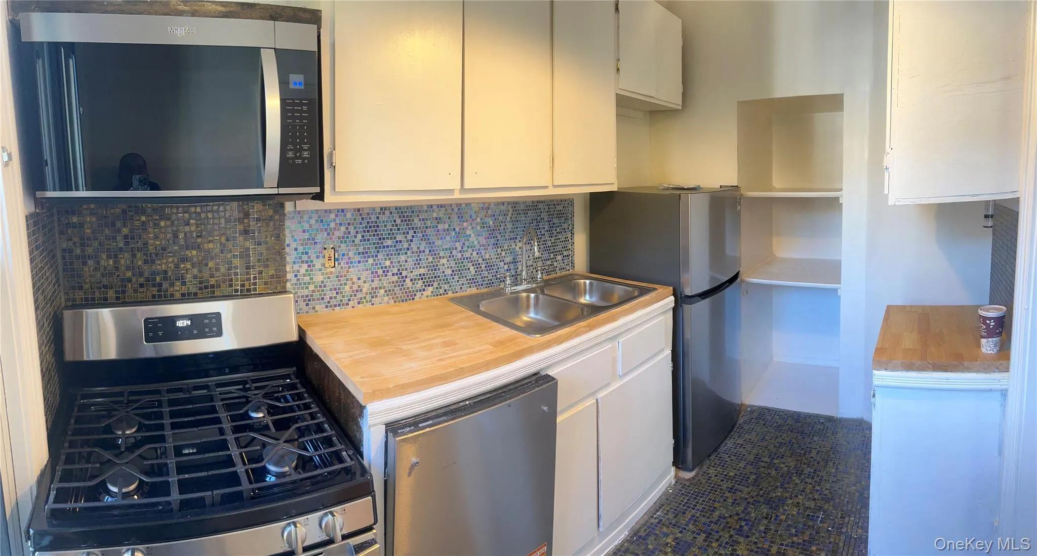 Kitchen featuring stainless steel appliances, butcher block countertops, backsplash, and white cabinetry Kitchen featuring stainless steel appliances, butcher block countertops, backsplash, and white cabinetry