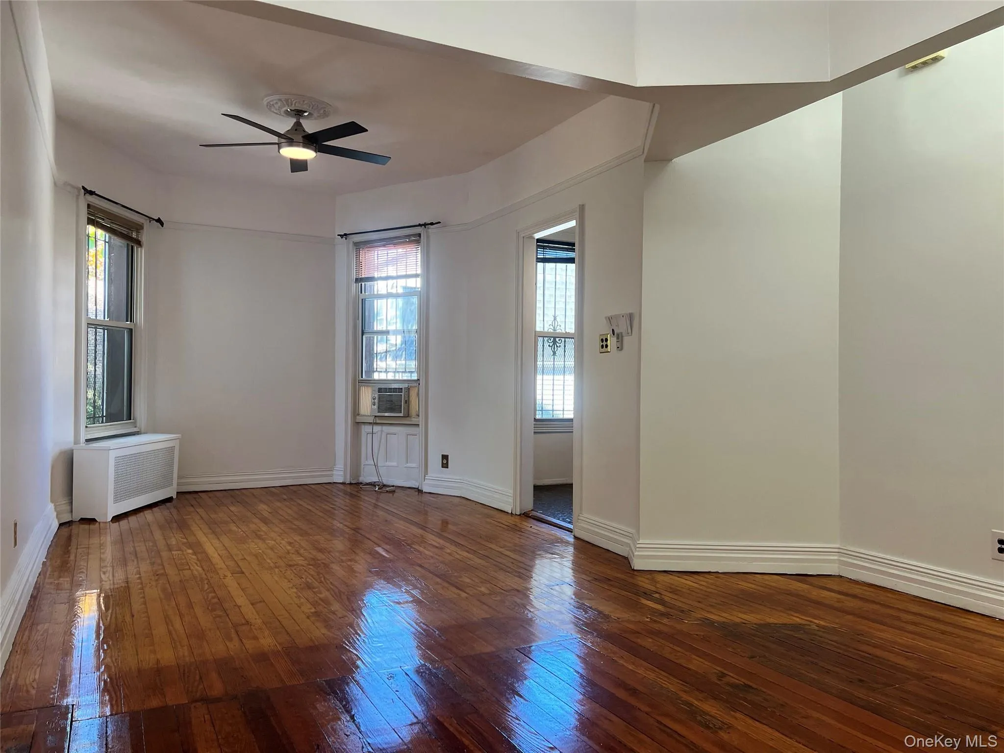Empty room with dark wood-style floors, ceiling fan, healthy amount of natural light, and radiator heating unit Empty room with dark wood-style floors, ceiling fan, healthy amount of natural light, and radiator heating unit