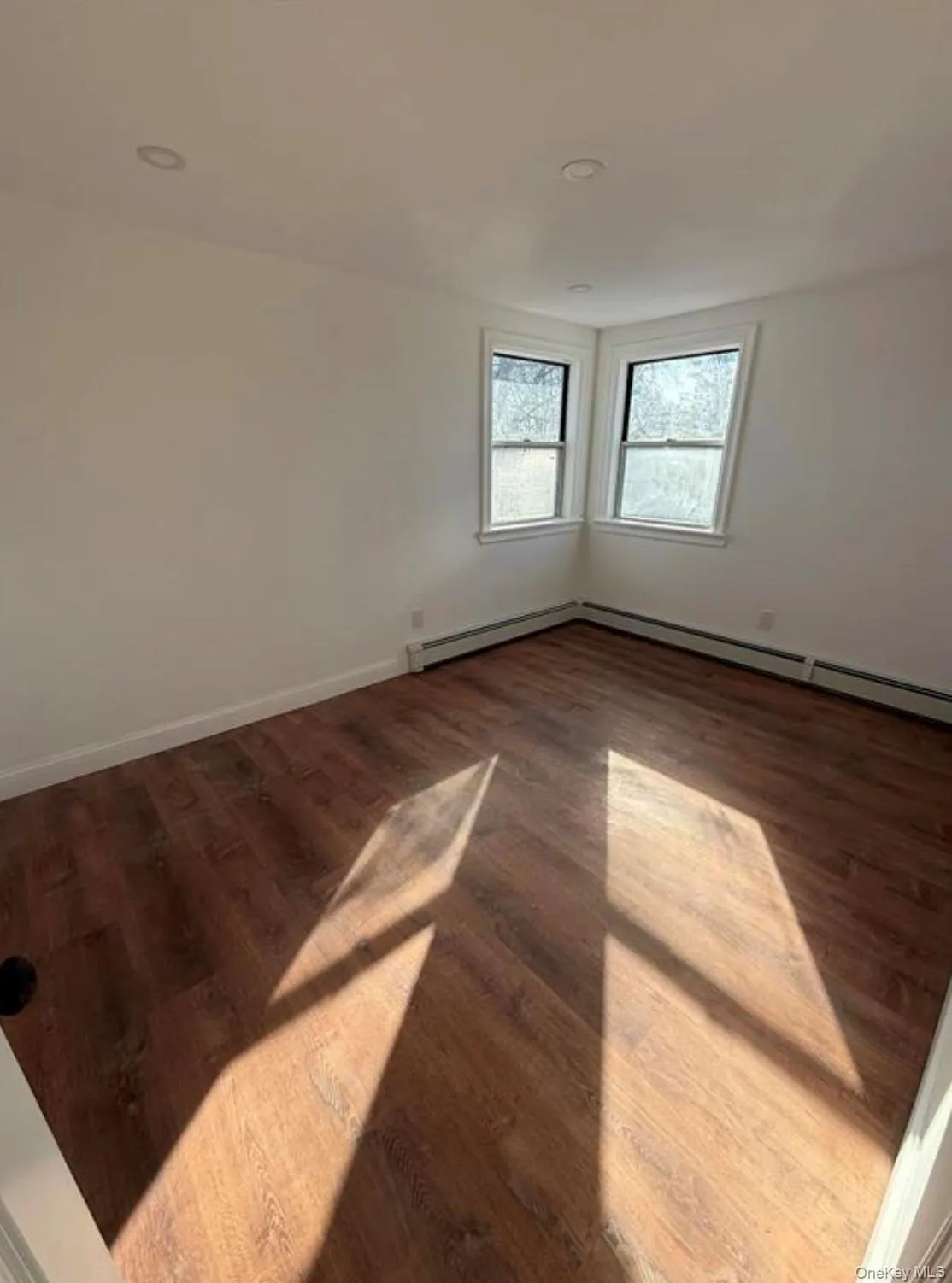 Unfurnished room featuring wood finished floors, baseboards, and a baseboard radiator Unfurnished room featuring wood finished floors, baseboards, and a baseboard radiator