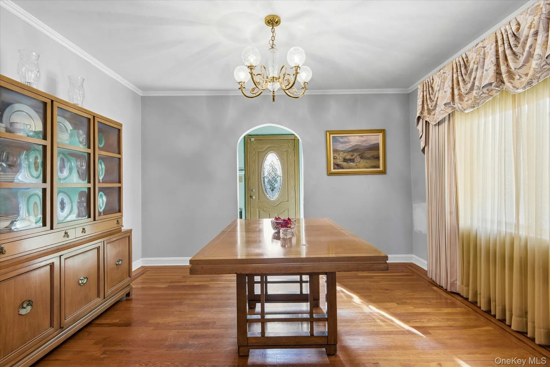 Dining room with crown molding, wood finished floors, a chandelier, and arched walkways Dining room with crown molding, wood finished floors, a chandelier, and arched walkways