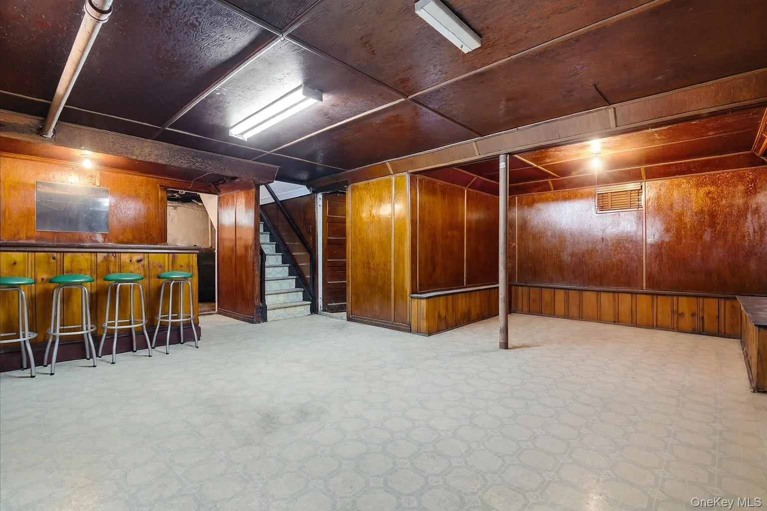 Finished below grade area with stairs, wooden walls, light flooring, and a bar Finished below grade area with stairs, wooden walls, light flooring, and a bar